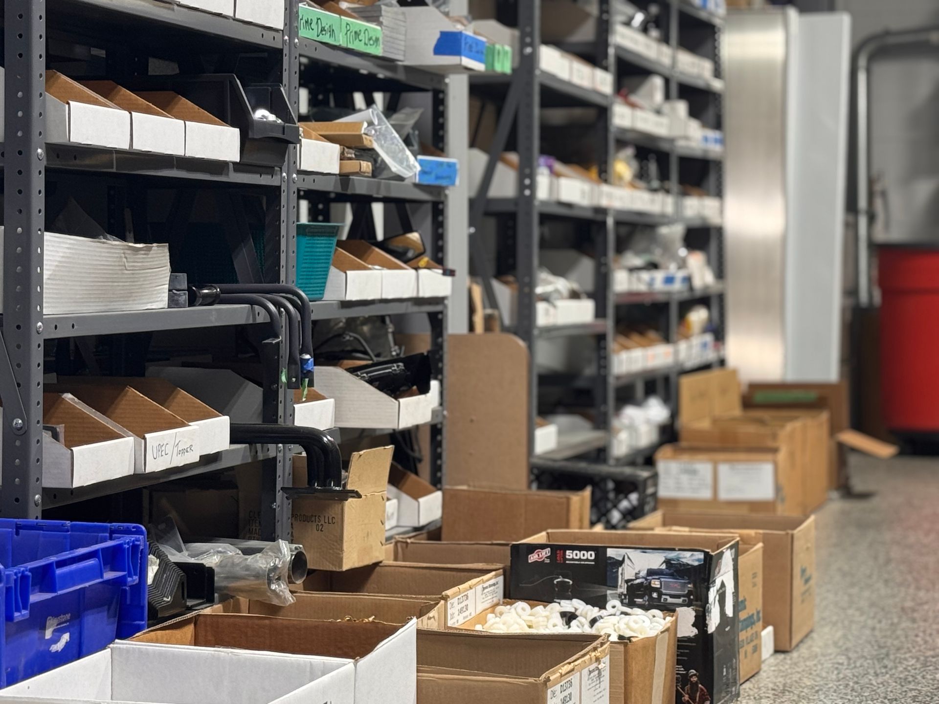 Shelves of boxed parts in a warehouse aisle with open cartons on the floor