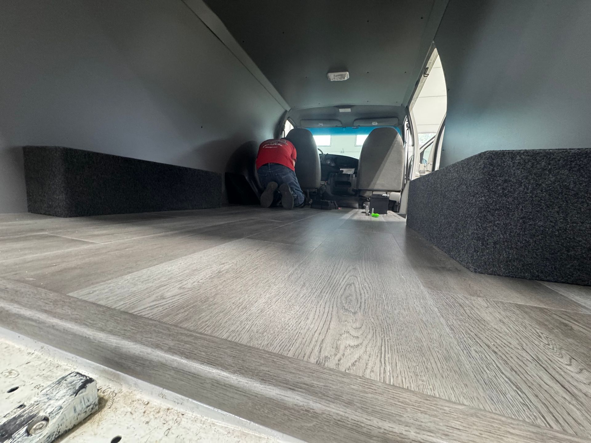 Low-angle view inside a van, showing a person in a red jacket working near the front seats.
