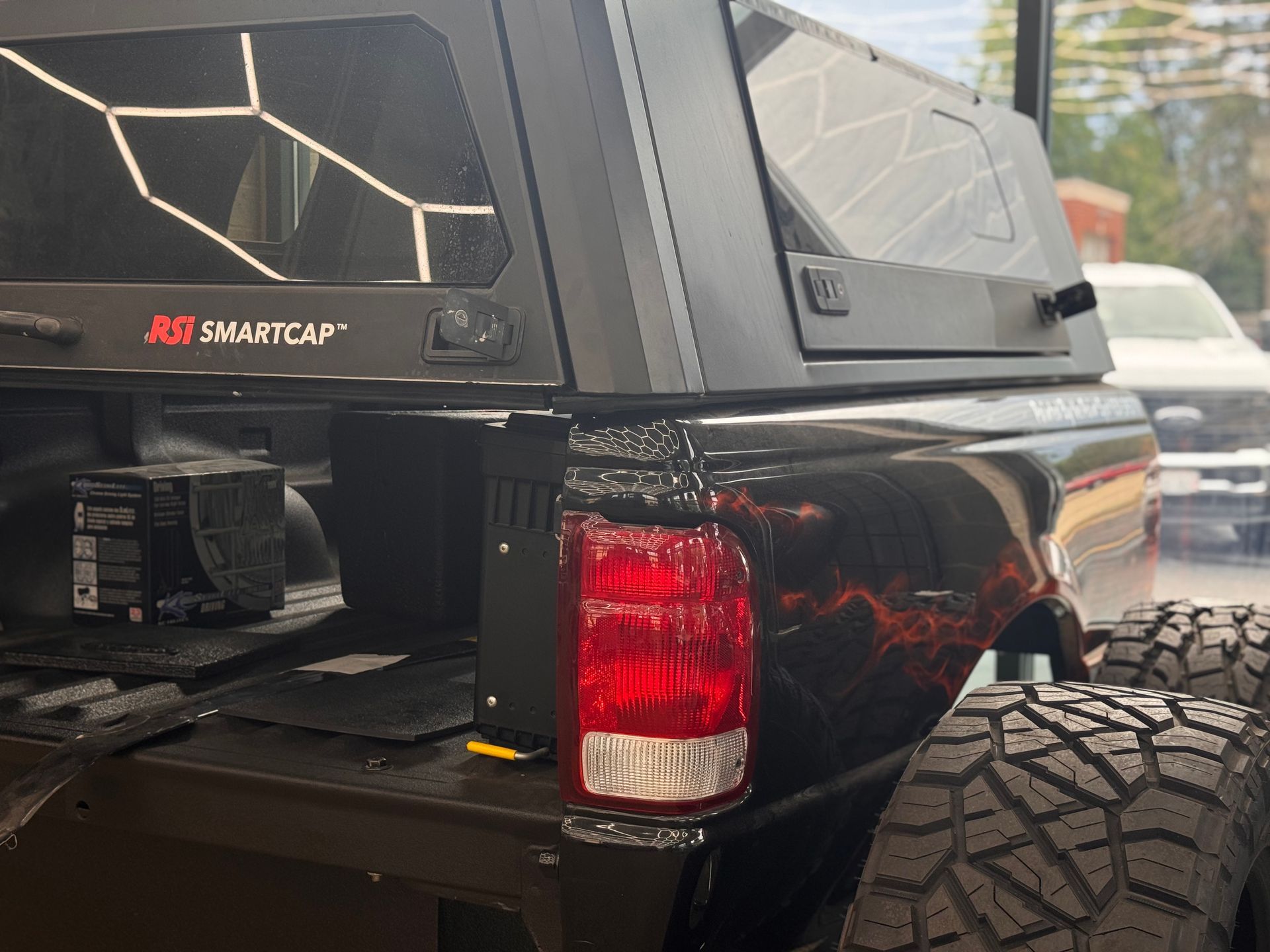 Black pickup truck bed with SmartCap canopy and red taillight, parked outdoors with large off-road tire visible