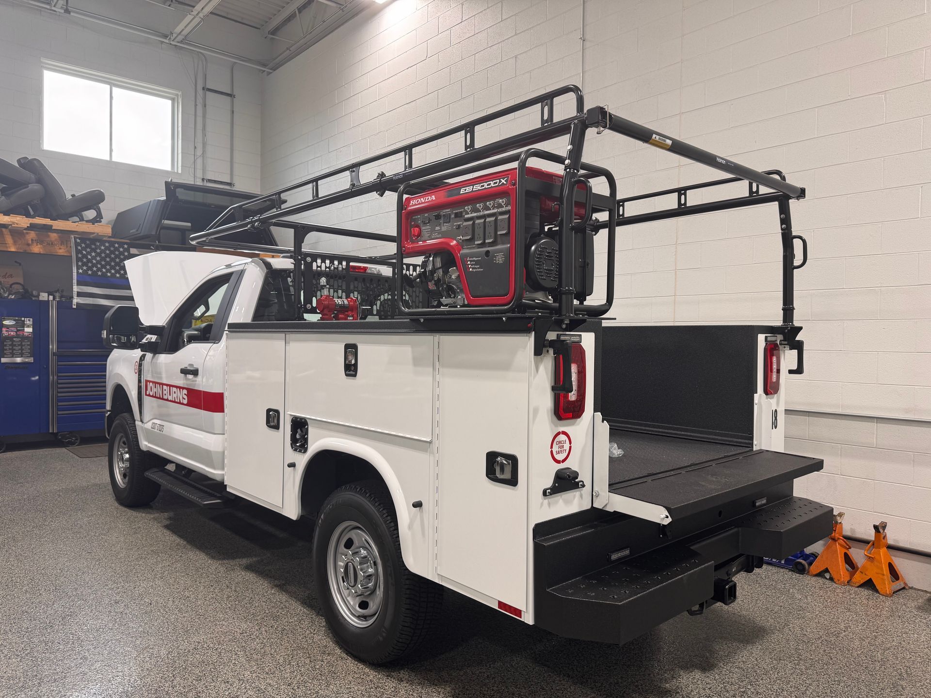 White utility truck with roof-mounted equipment parked inside a garage bay.