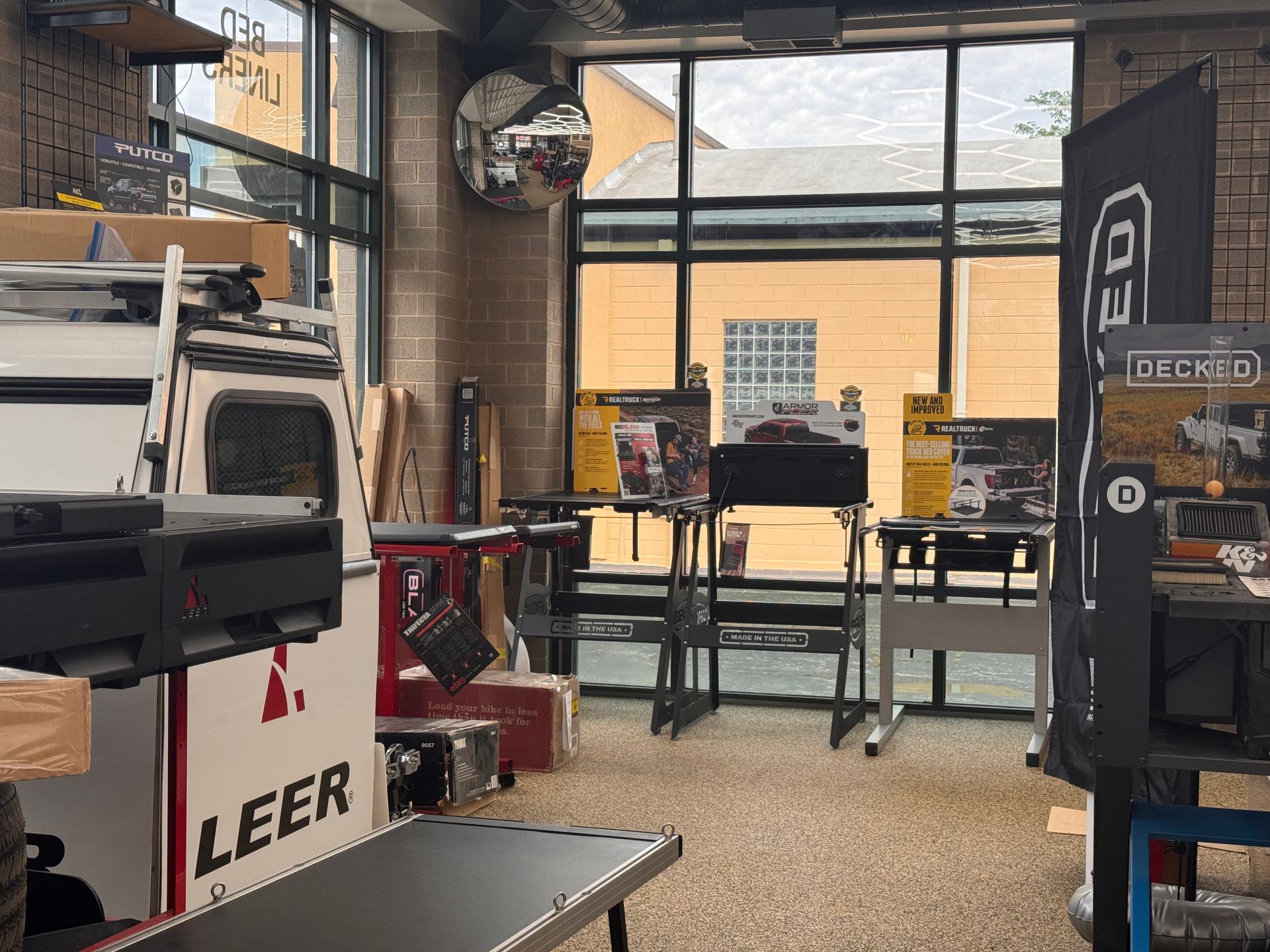 Truck accessories showroom with camper shells, racks, and display tables near large windows