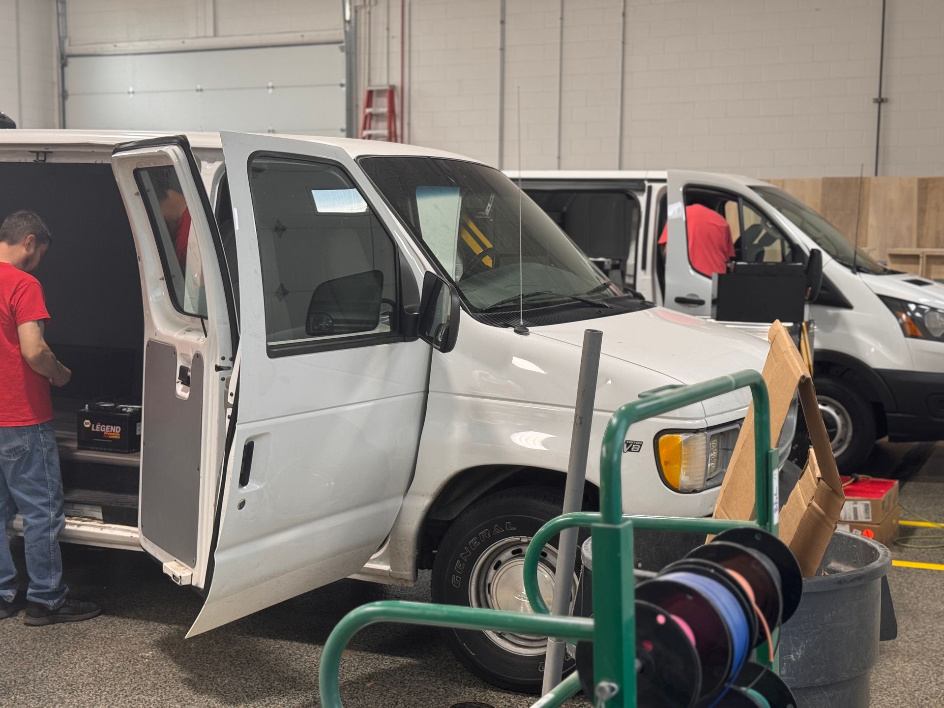 White work van with open doors in a warehouse, with a person nearby and a hose reel in the foreground.