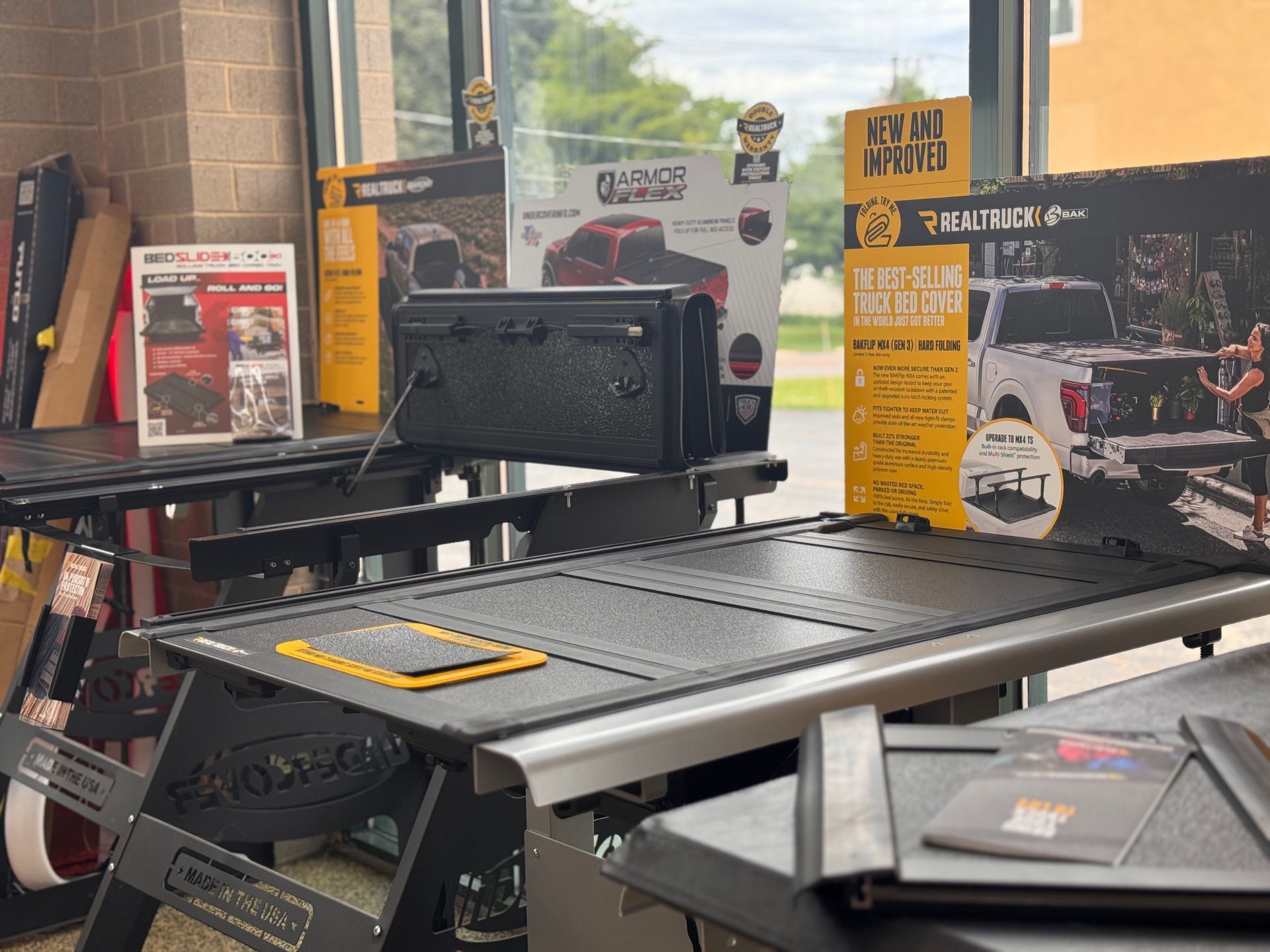 Display of a black folding table and equipment brochures in a showroom, with a window and outdoor view behind.