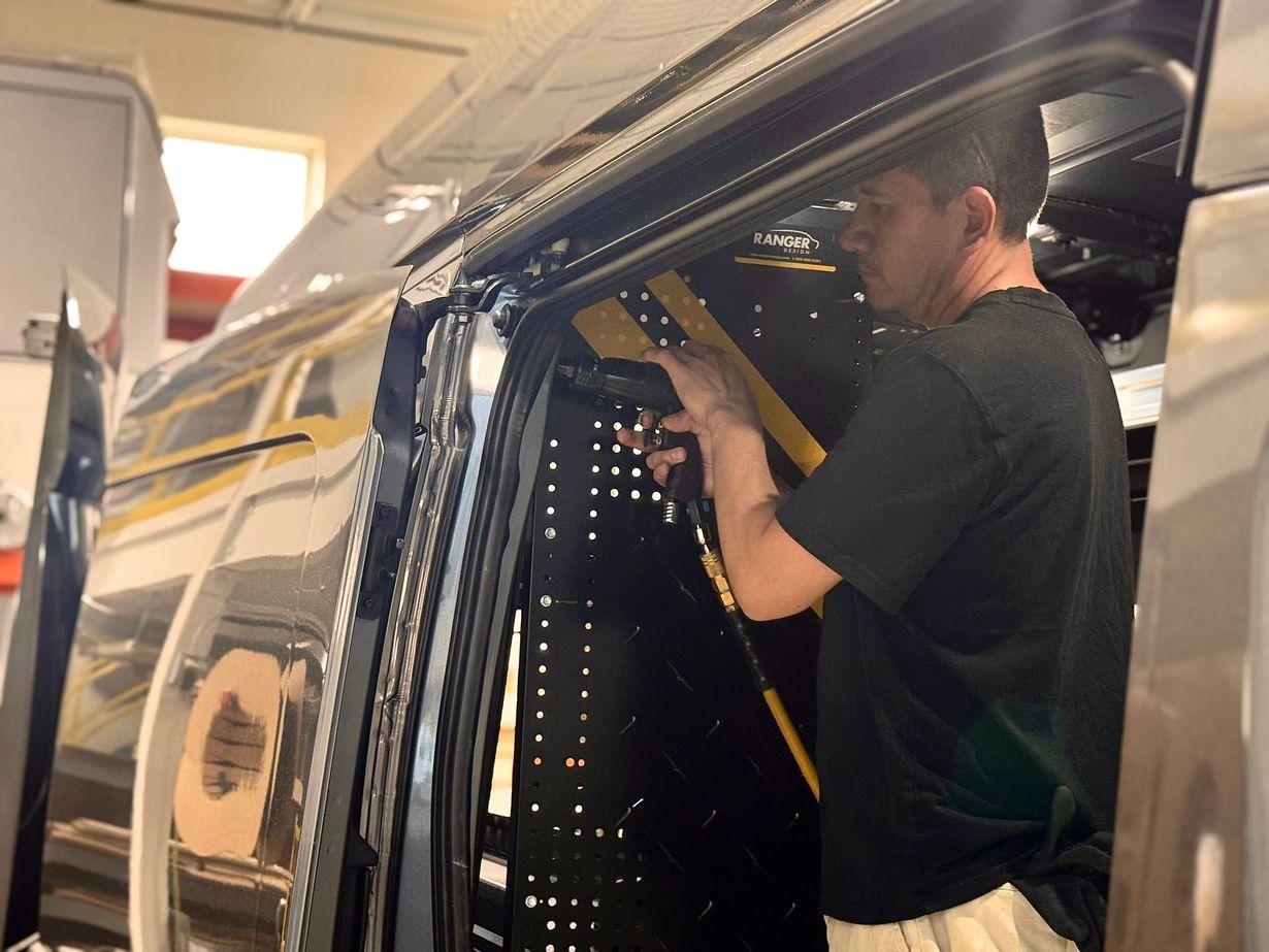Technician installing wiring inside a vehicle door frame in a workshop