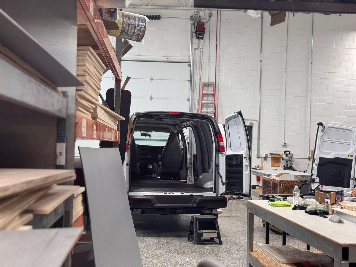 Black SUV parked inside a cluttered auto repair shop with tools, shelves, and a lift.
