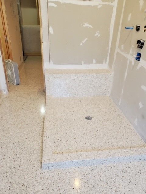 A bathroom with a walk in shower and a fan on the floor.