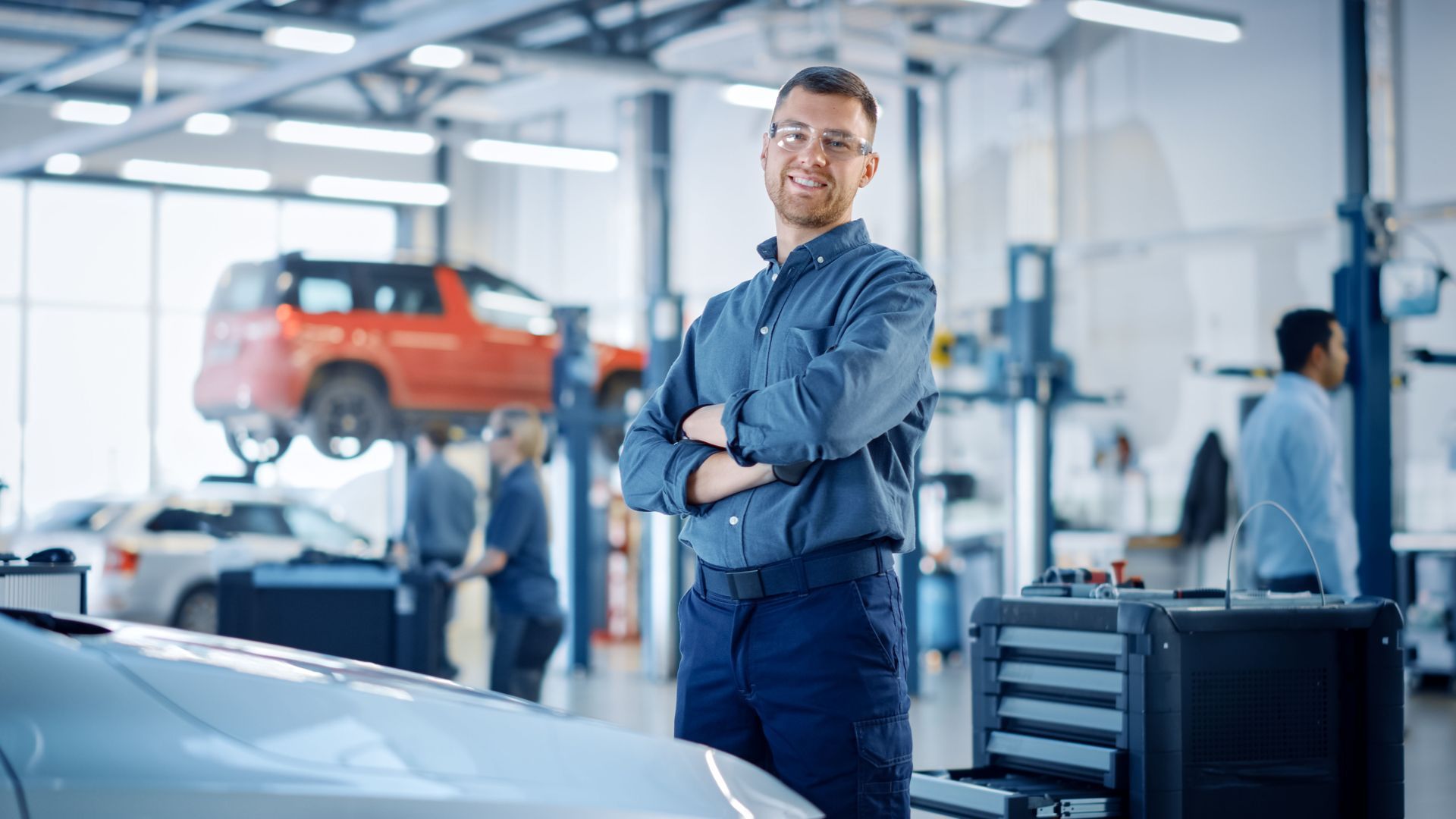 A man is standing next to a car in a garage with his arms crossed.