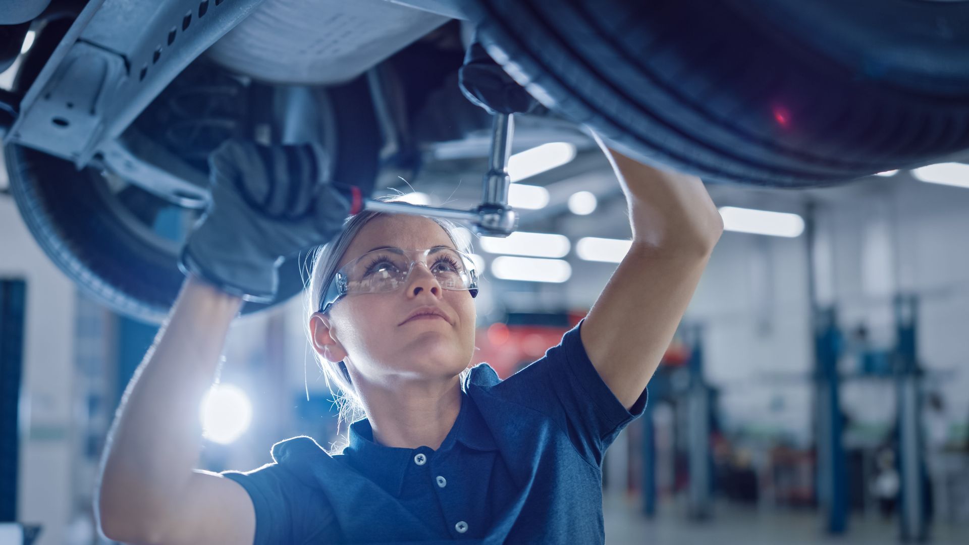 A woman is working underneath a car in a garage.