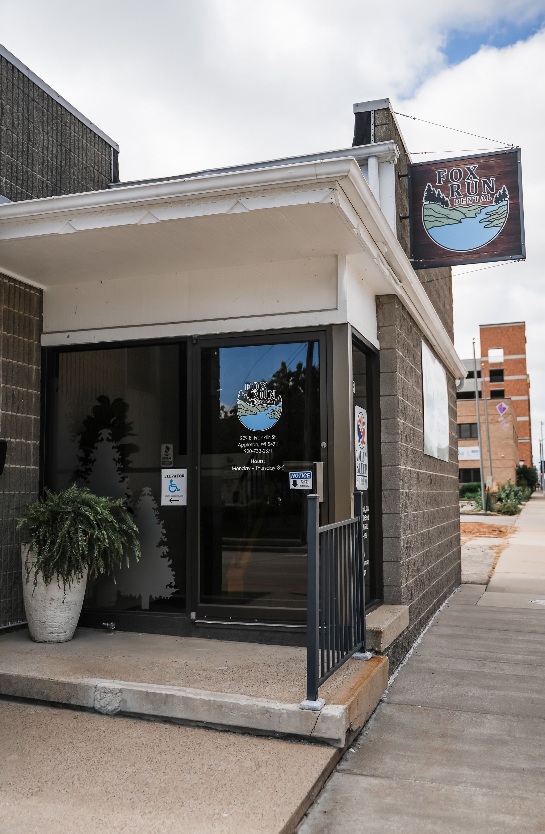 Entrance to a business with sign, glass door, brick facade, and accessible entrance symbol.