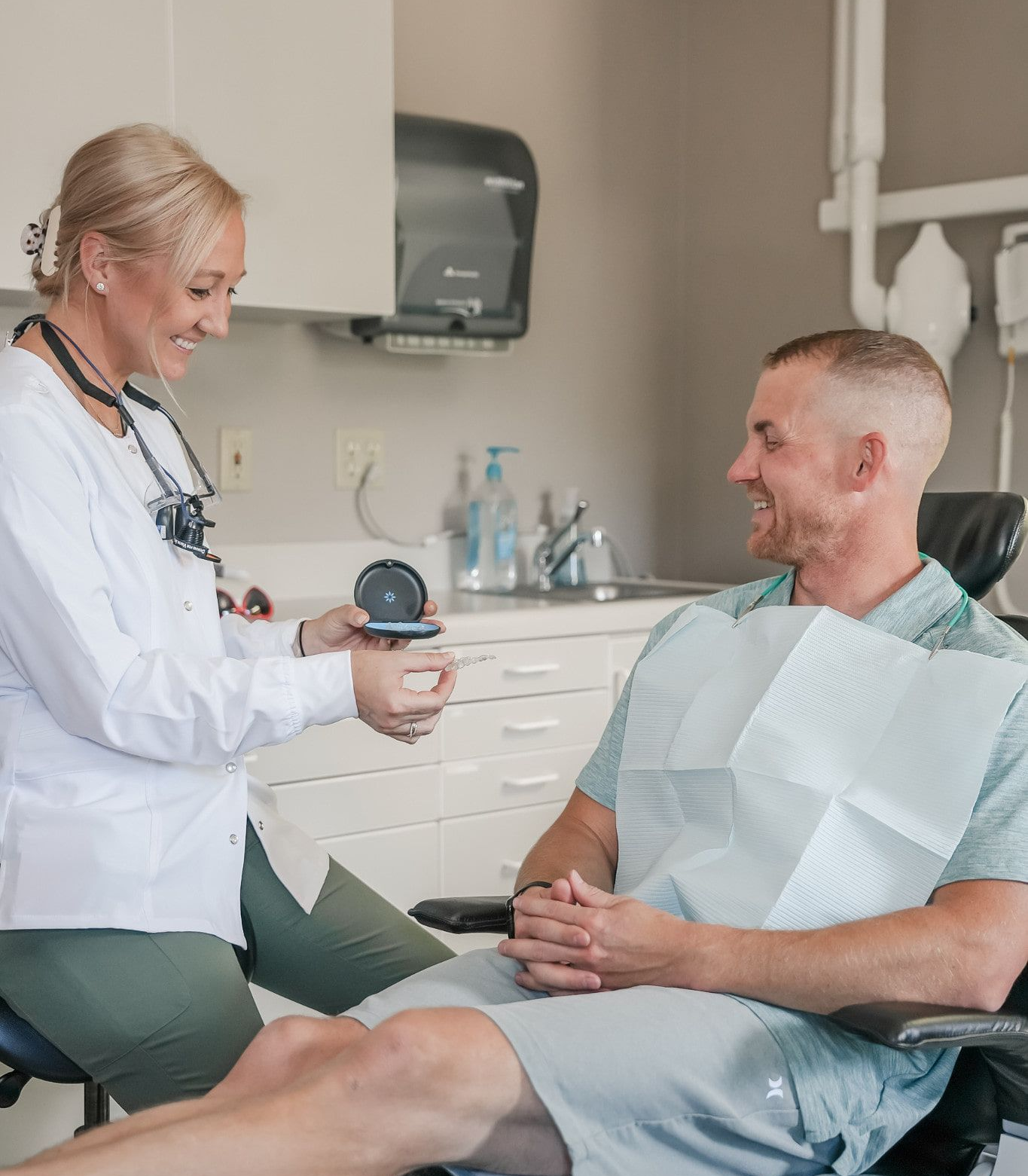 A dentist shows a patient a small device in a dental office. Both smiling.