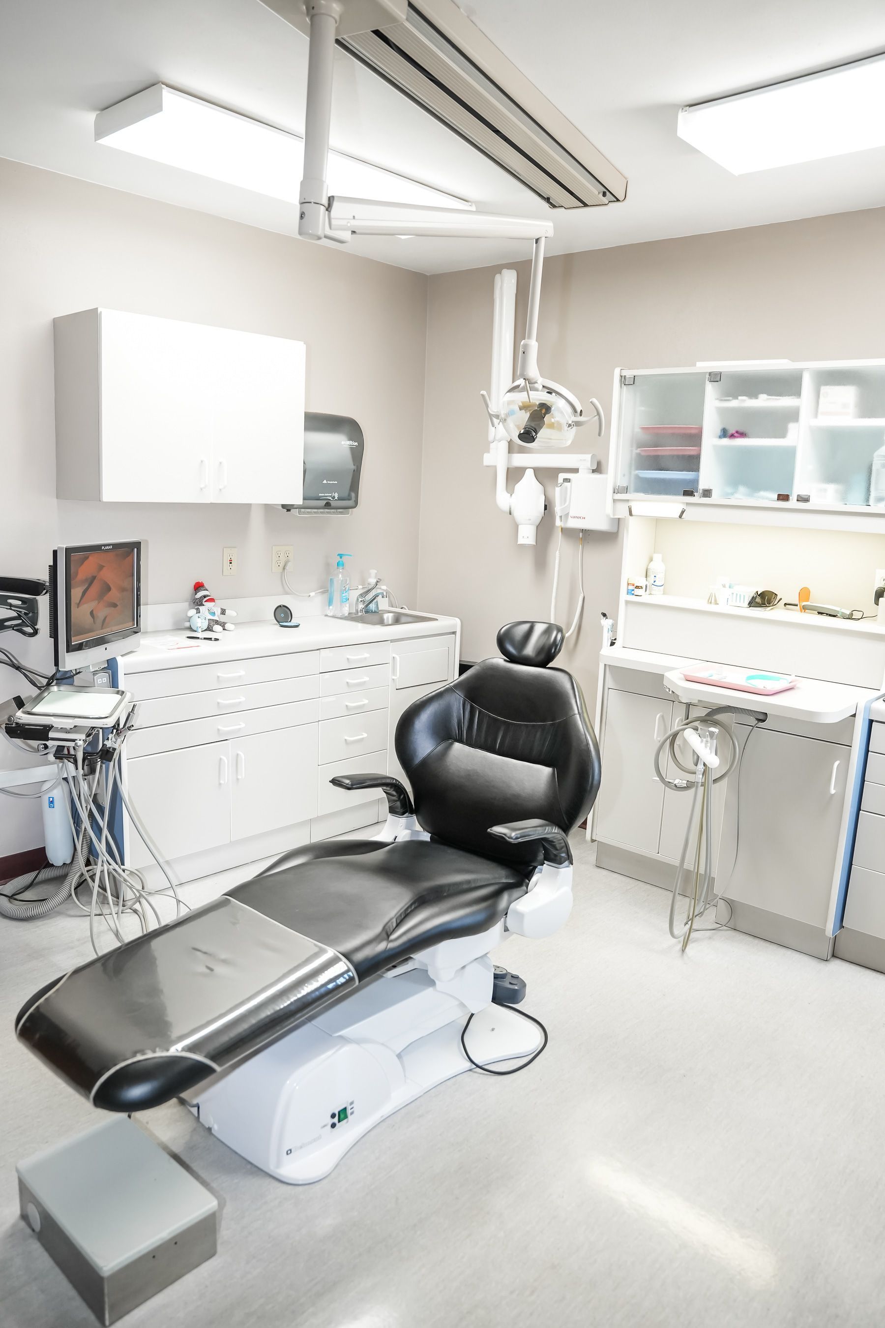 Dental office interior with patient chair, cabinets, and overhead light fixture.