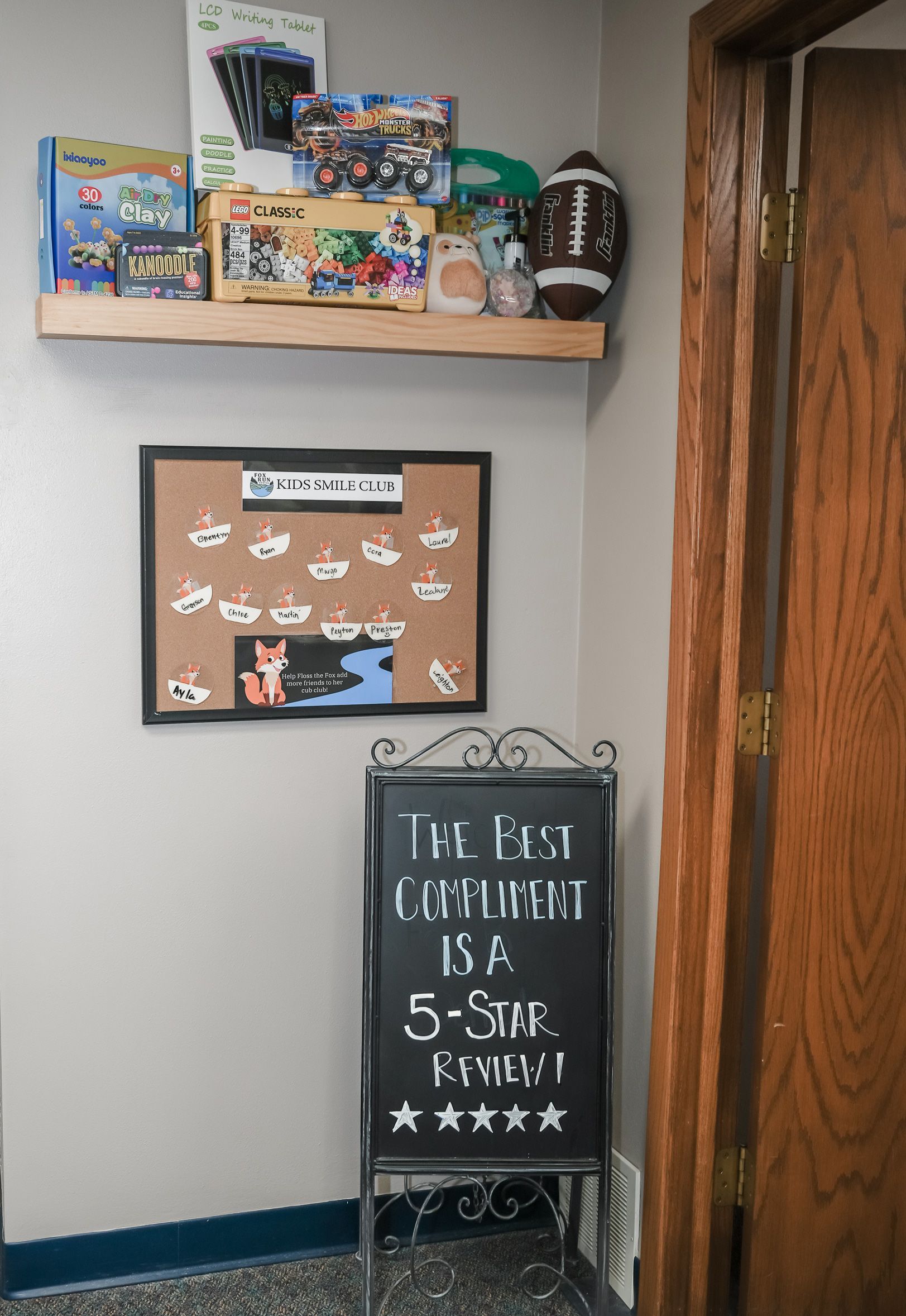 Corner of the room with a shelf of toys, a cork board with drawings, and a chalkboard sign.