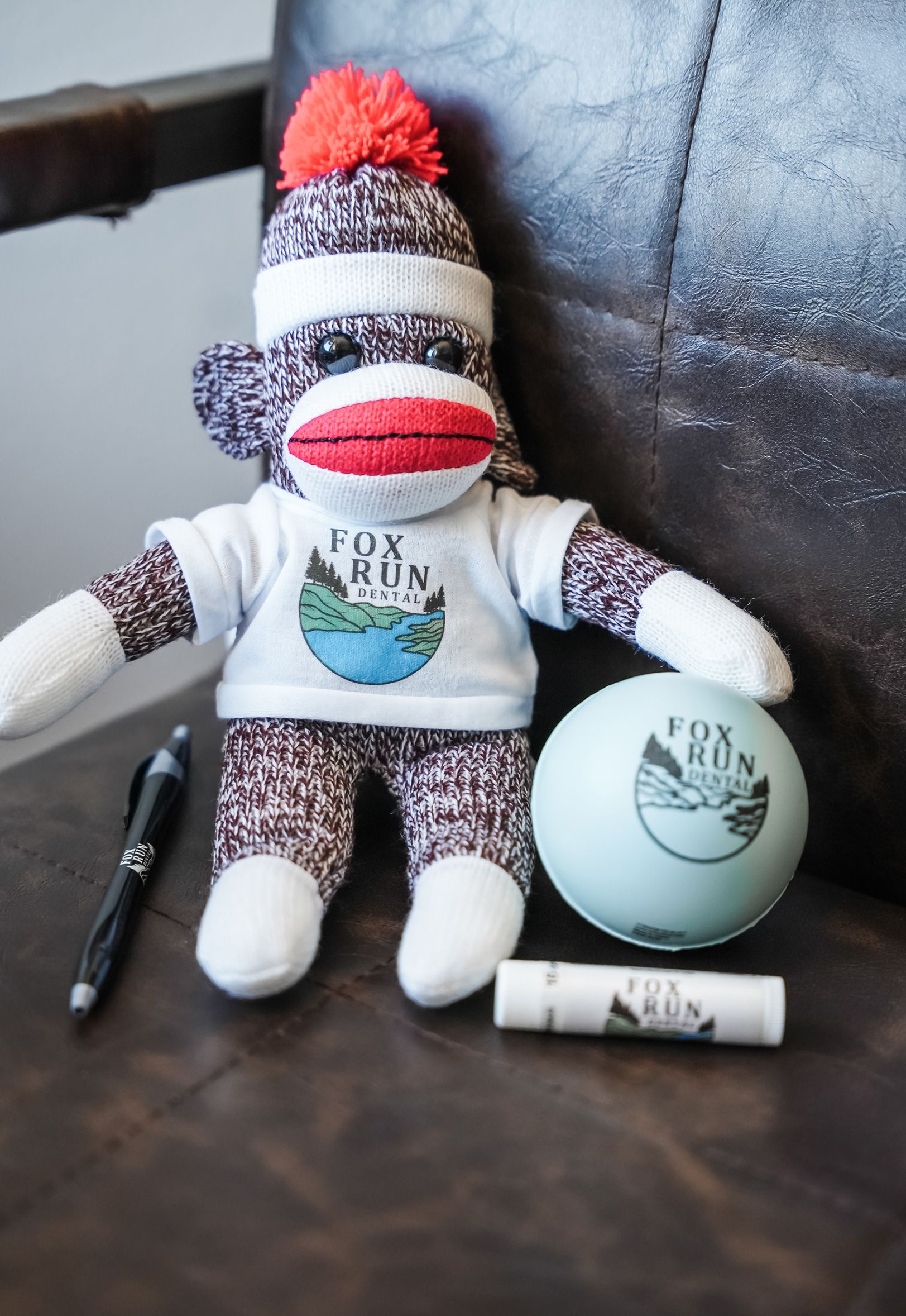 Sock monkey wearing a Fox Run t-shirt next to a stress ball, pen, and lip balm.