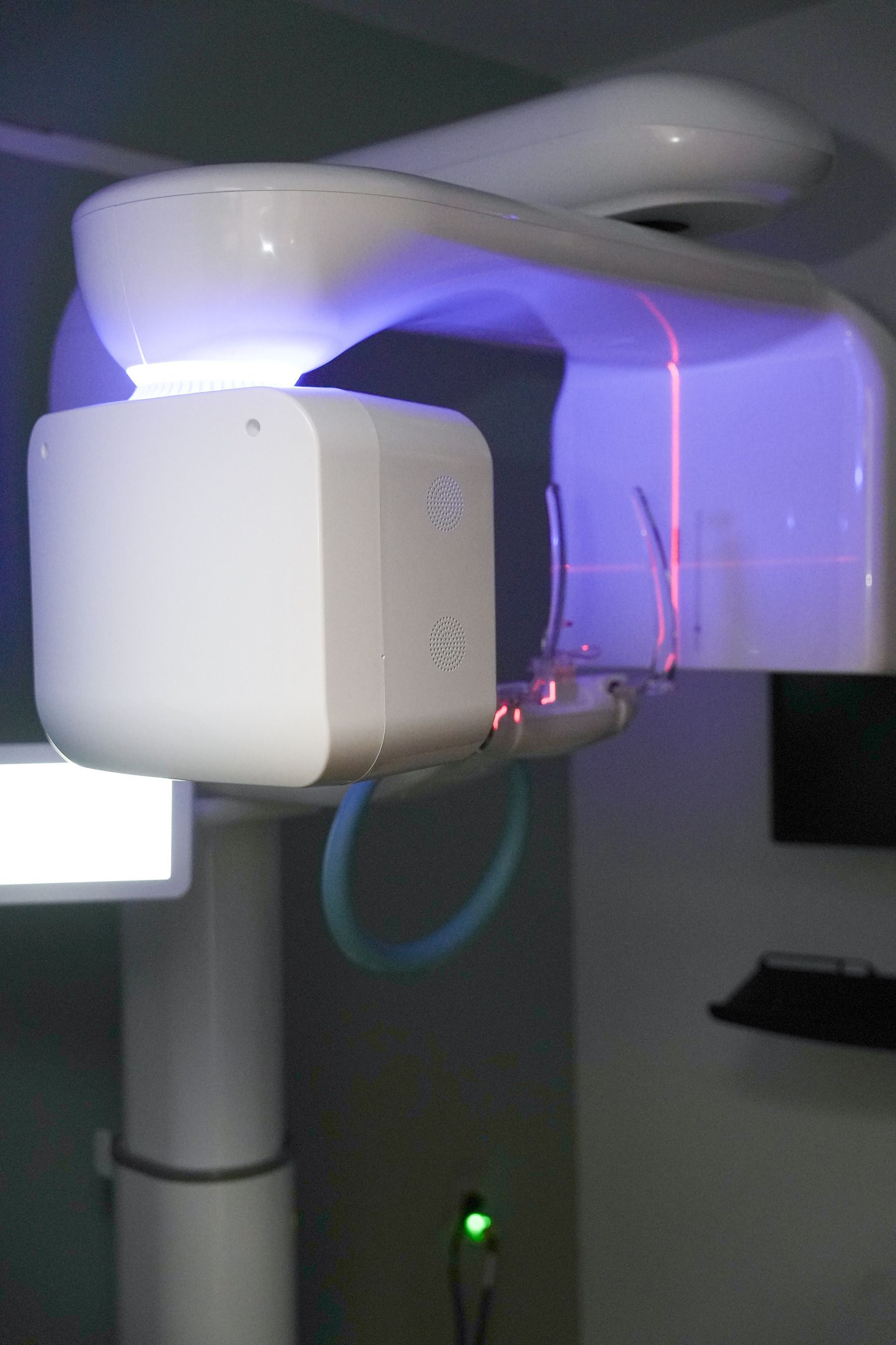 Panoramic dental X-ray machine with blue lights, red laser, and green power indicator in a dental office.