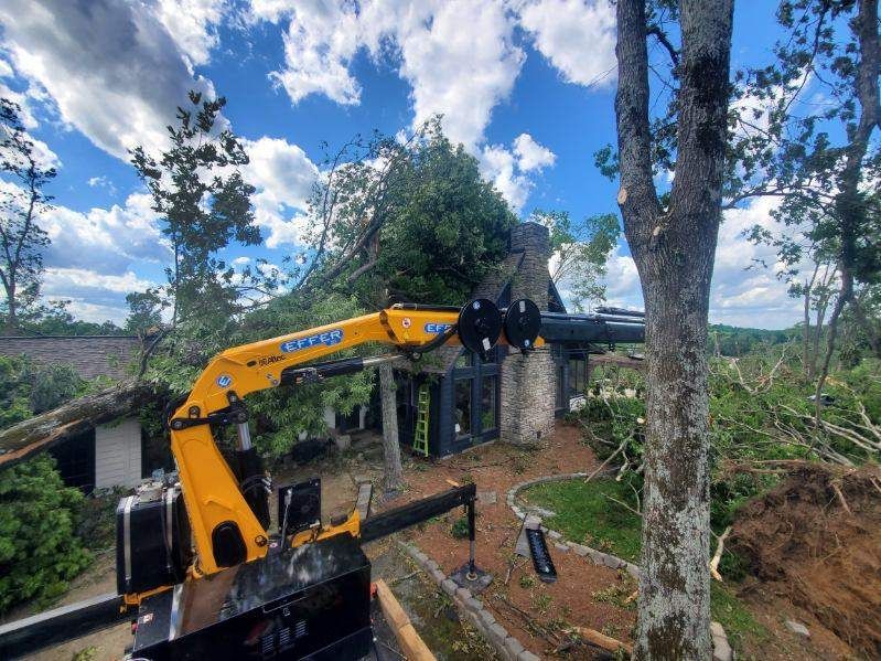 A crane is cutting down a tree in front of a house.