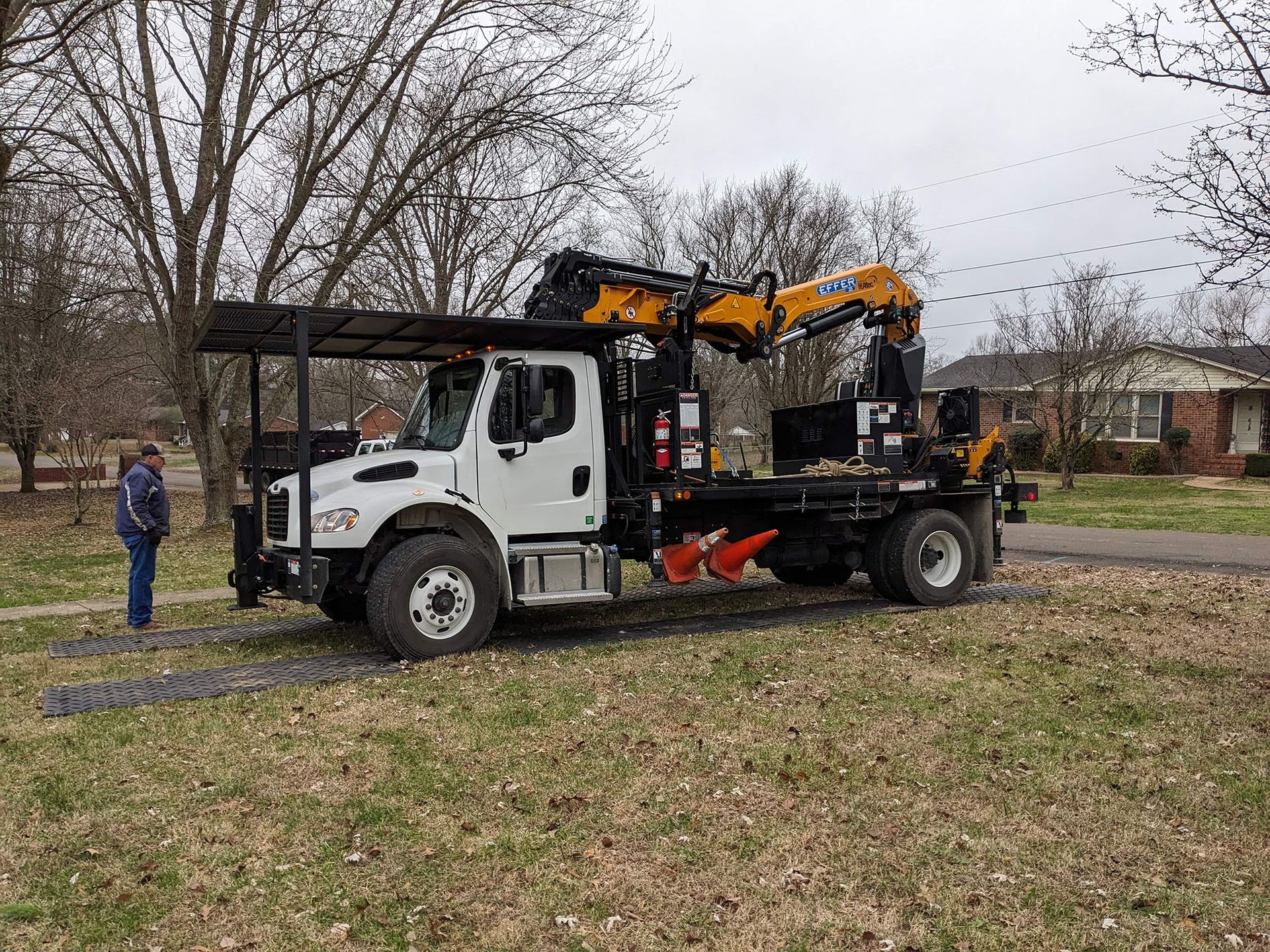 A white truck with a yellow crane on the back is parked in a grassy field.
