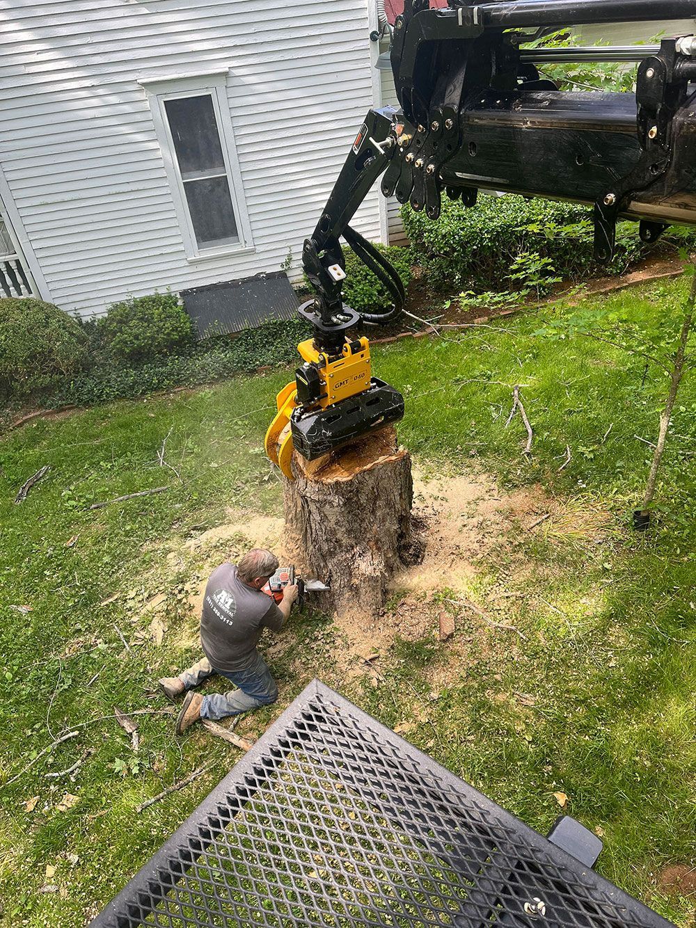 A man is kneeling down next to a tree stump in a yard.