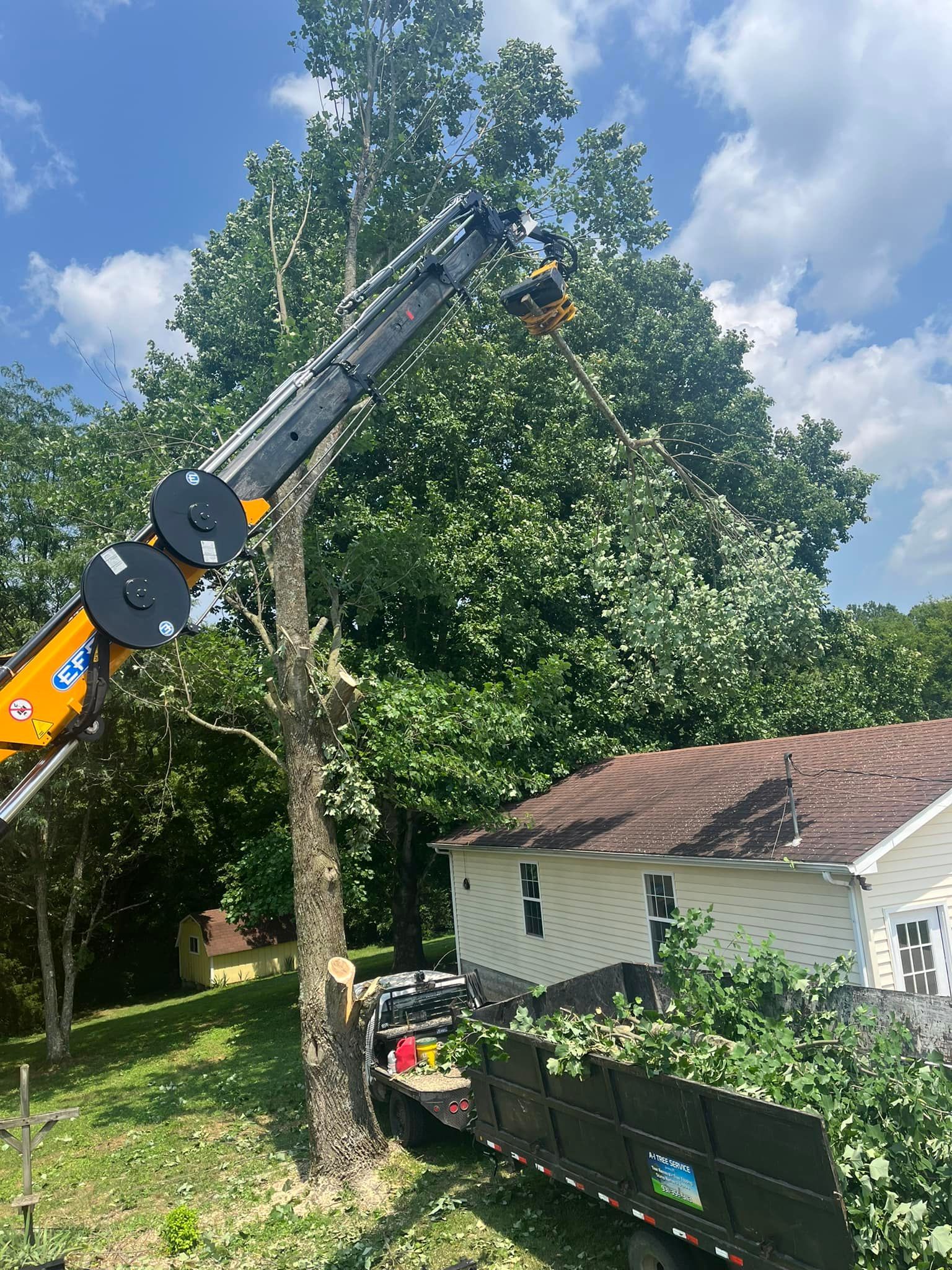 A crane is cutting a tree in front of a house.