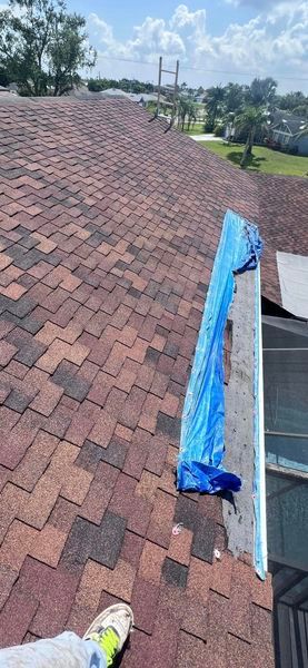 A person is standing on a roof with a blue tarp on it.
