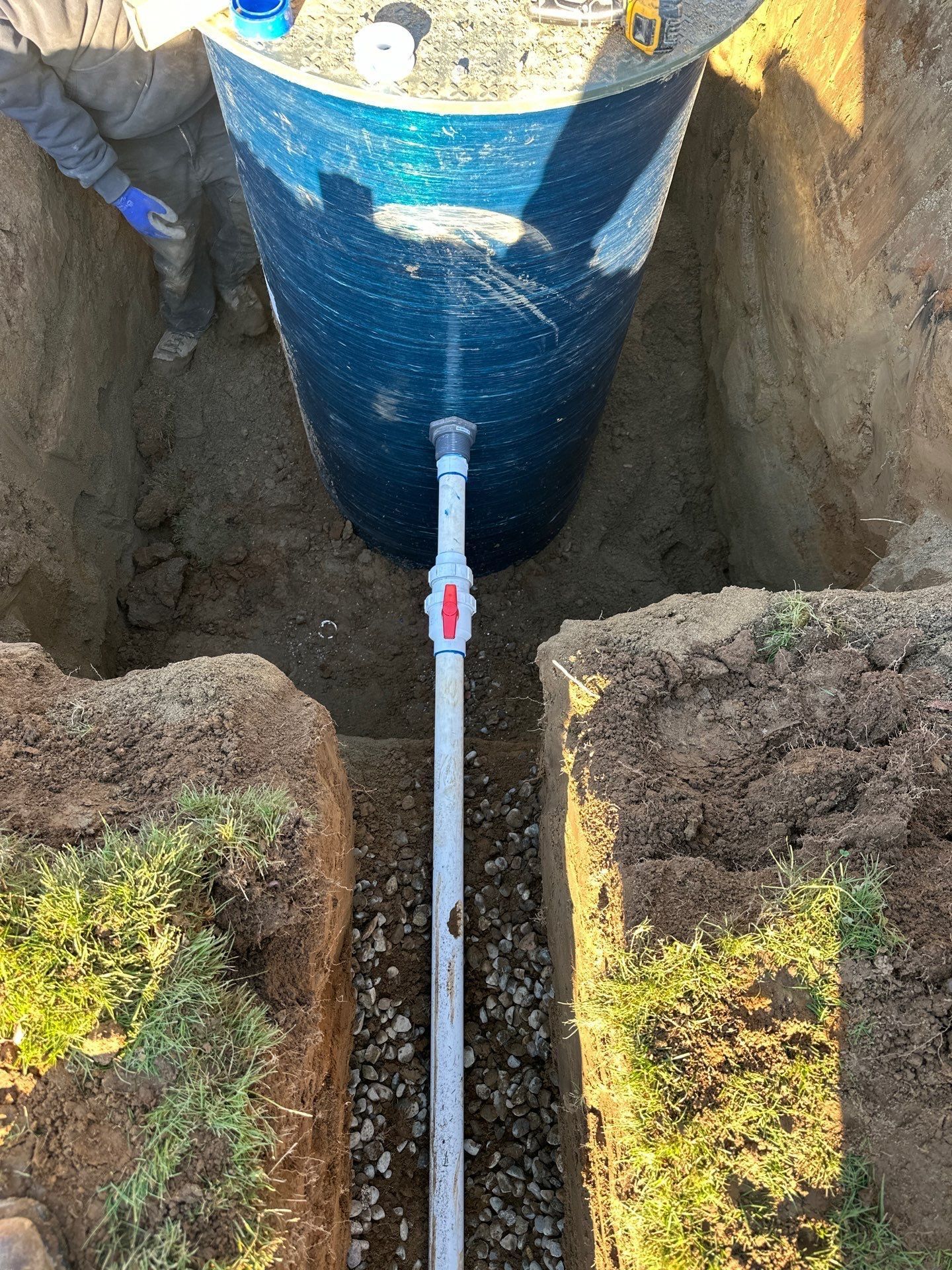 Blue cylindrical utility pipe in a trench, connected to a valve and white pipe between two soil walls.