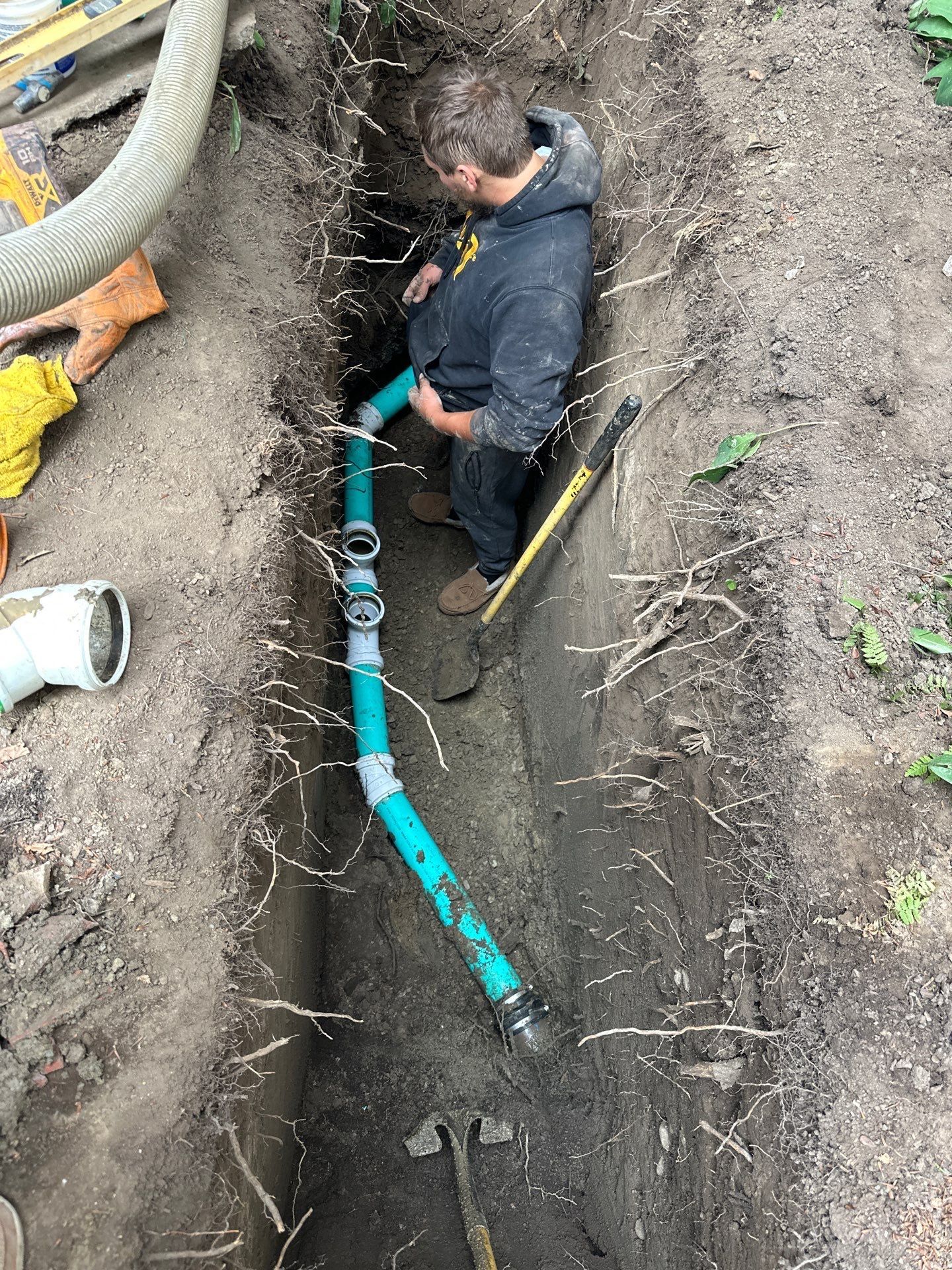 Worker repairing blue pipes in a narrow trench outdoors.
