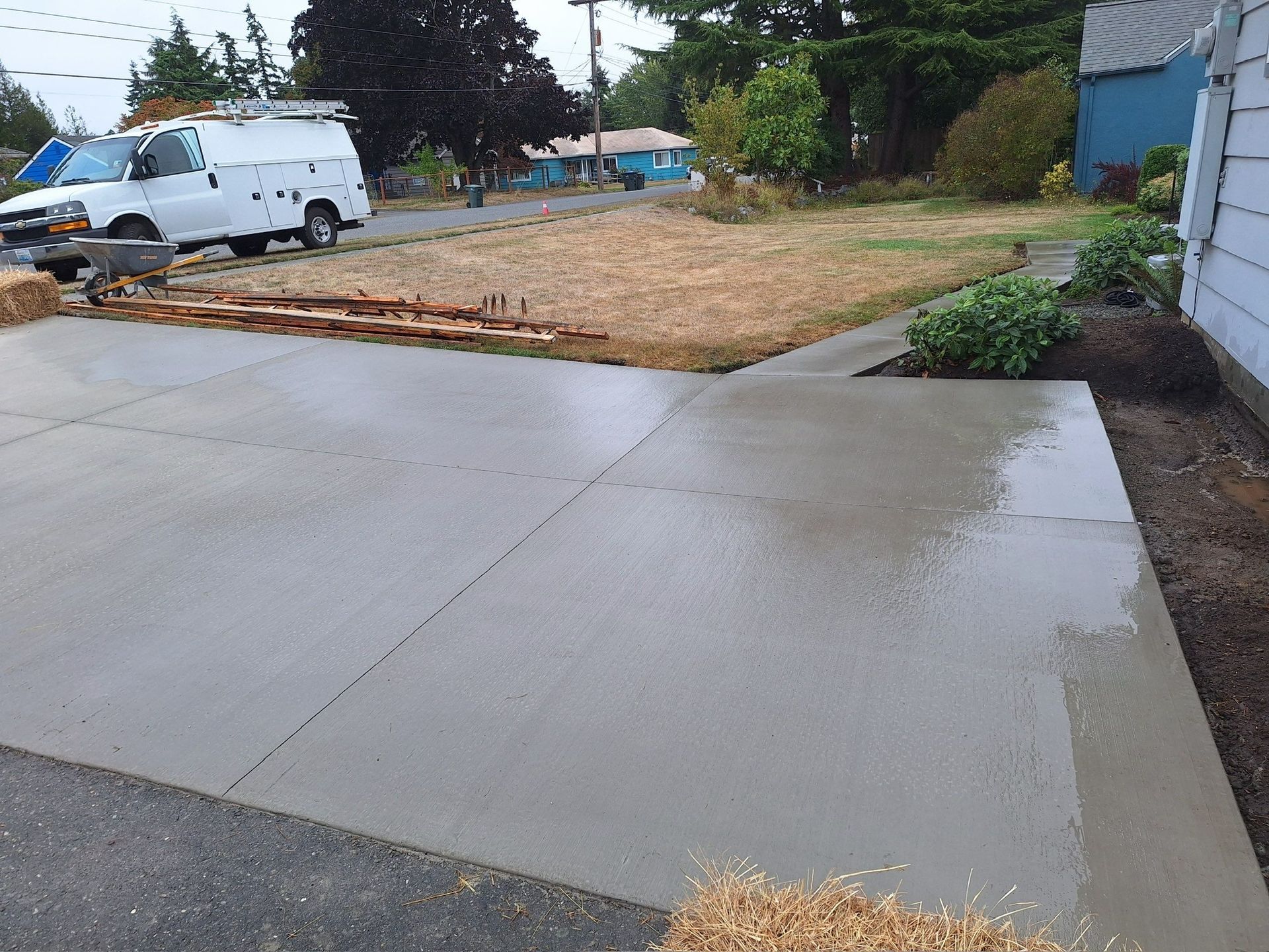 Freshly poured concrete driveway beside a dirt lot with a white van in the background.