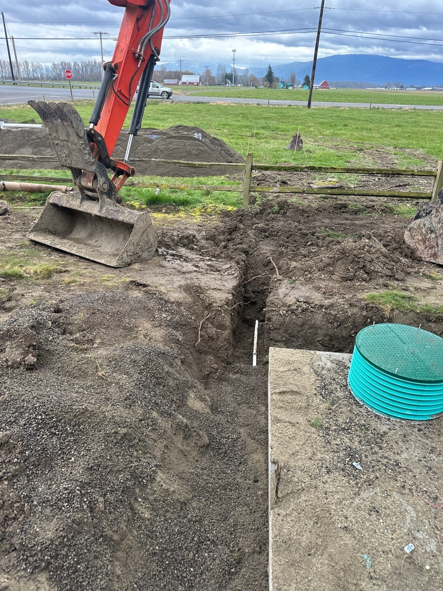 Excavator digging a trench beside a concrete slab on a muddy construction site.