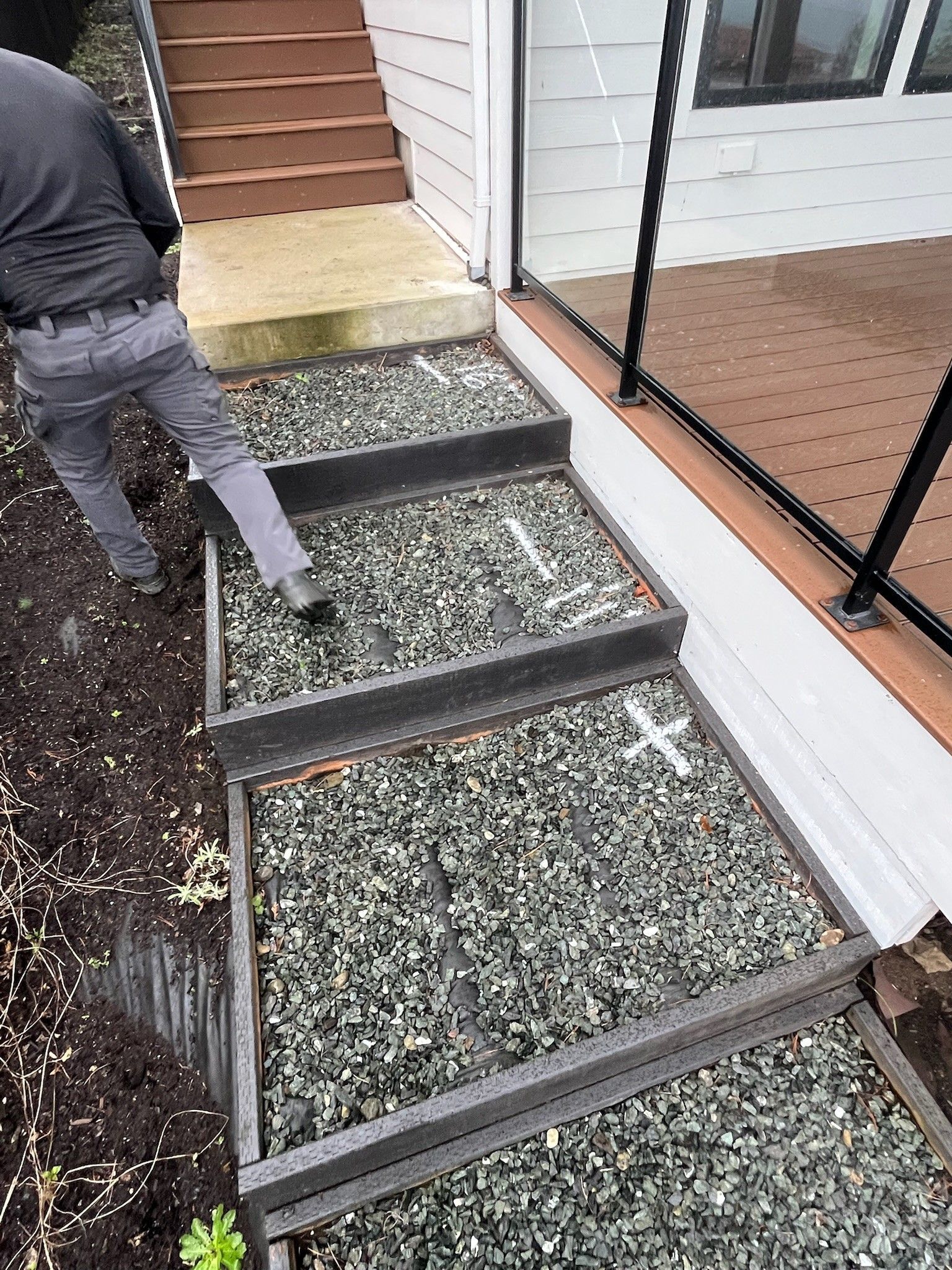 Person walking up gravel steps beside a house entrance with a glass railing.
