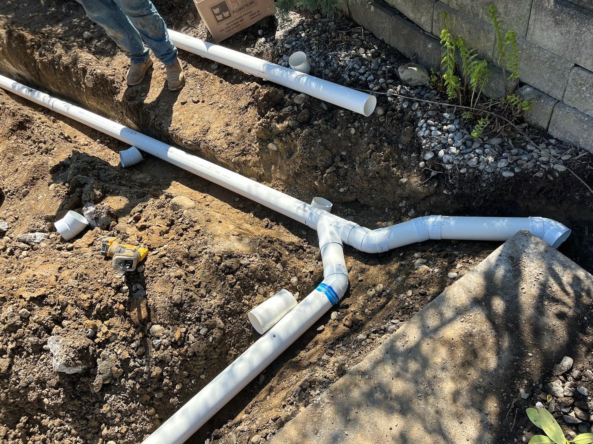 Broken white PVC pipes in a dirt trench during outdoor plumbing work.