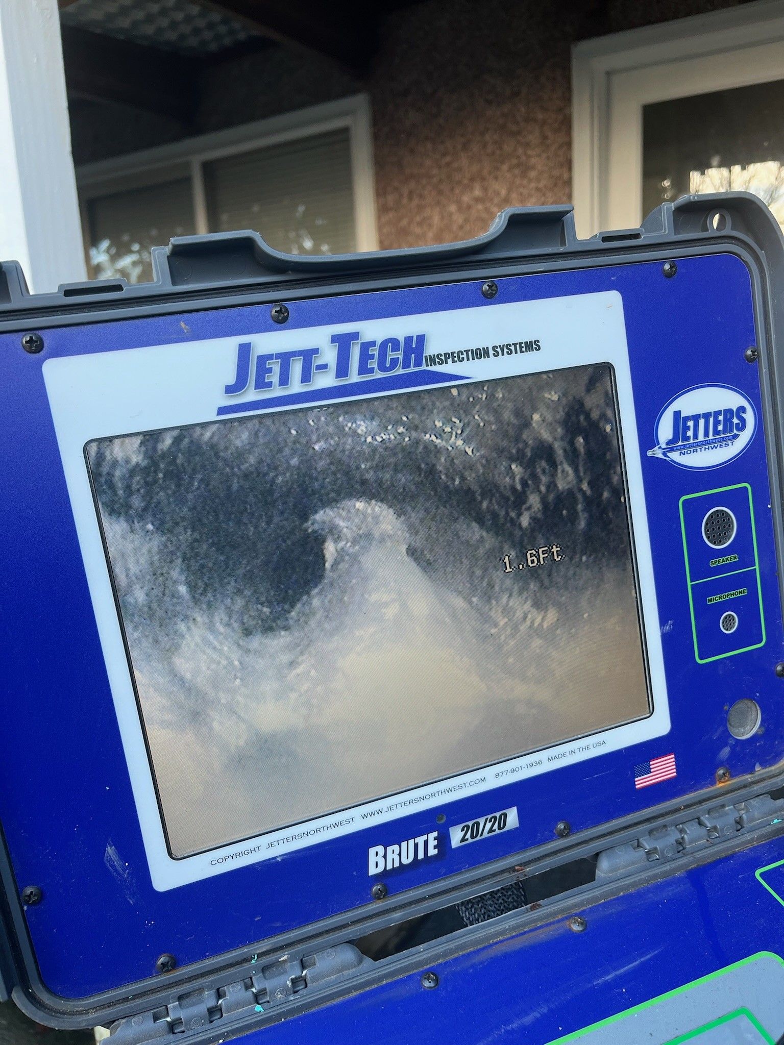 Blue Jet-Tech handheld inspection monitor showing a blurry black-and-white image outdoors.