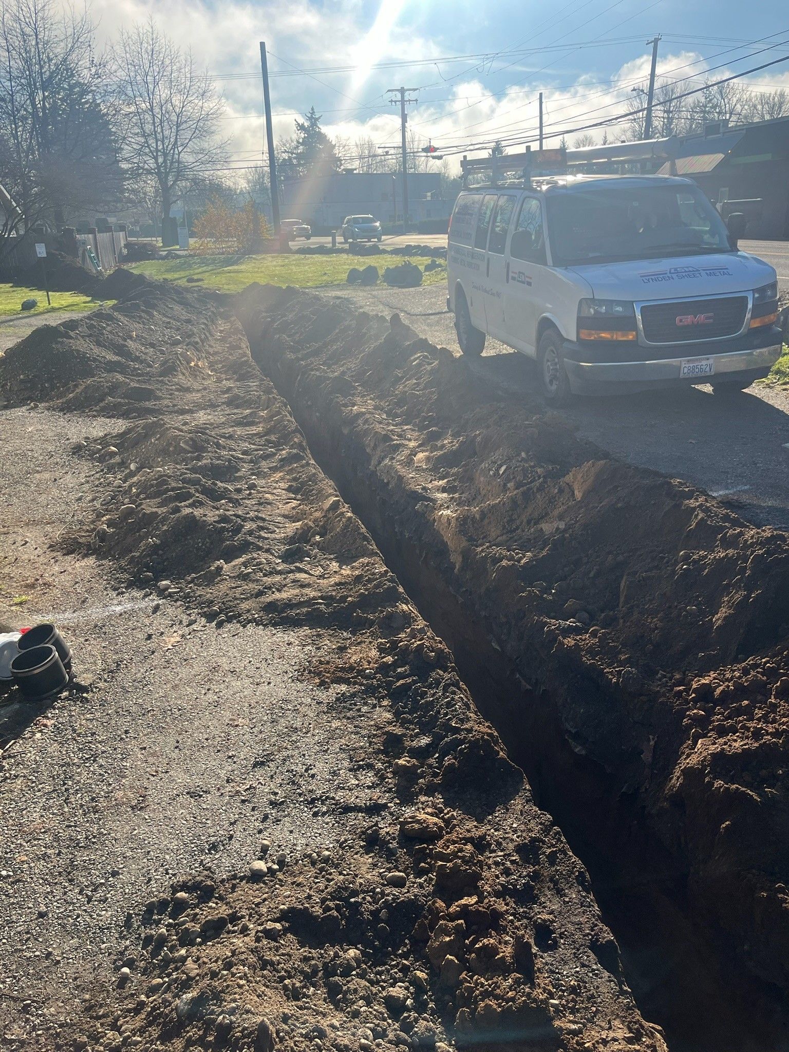 Road trench under construction beside a white truck on a sunny residential street.