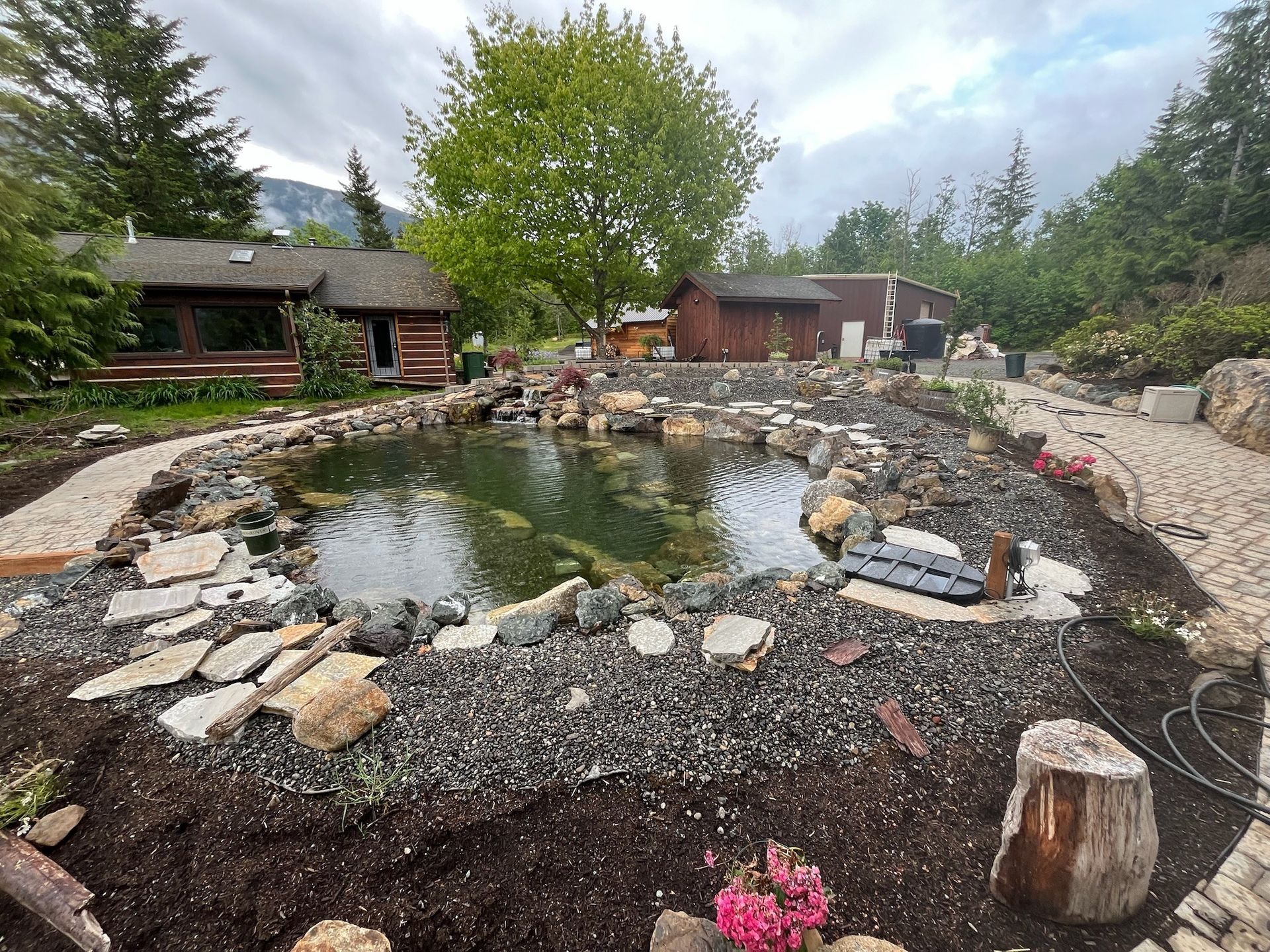 Rock garden with a small pond, stone border, and surrounding trees and rustic cabins.