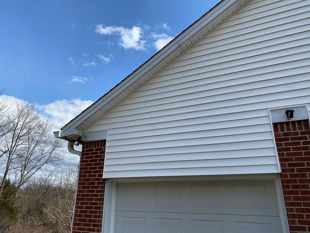 A white siding on a brick house with a white garage door.