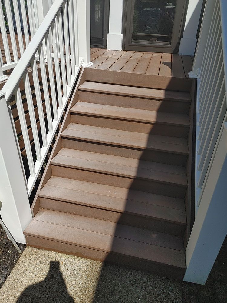 A set of wooden stairs leading up to a deck with a white railing.