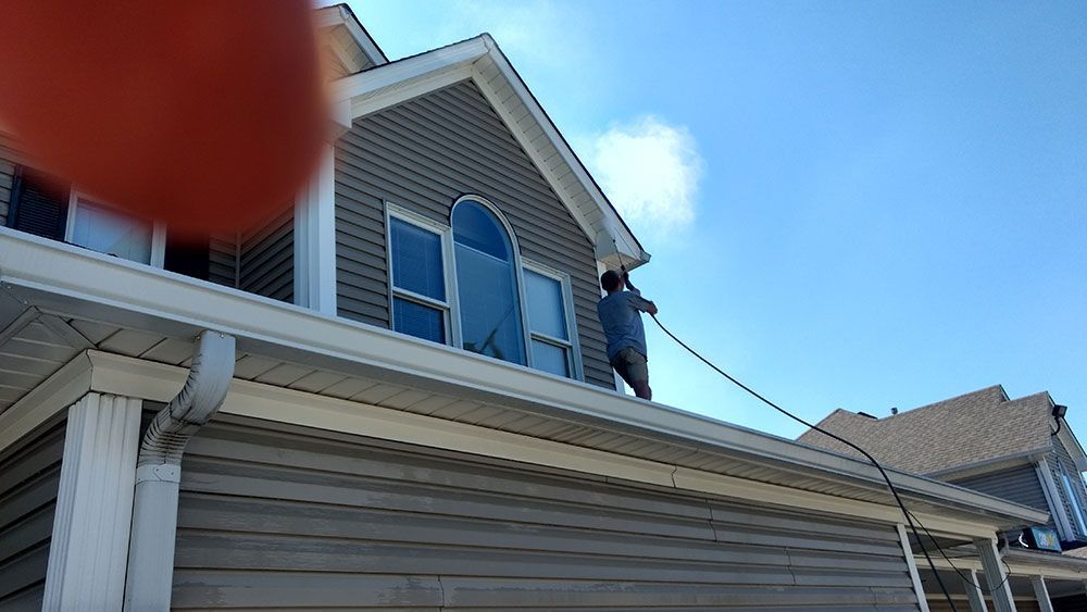 A man is cleaning the roof of a house with a hose.