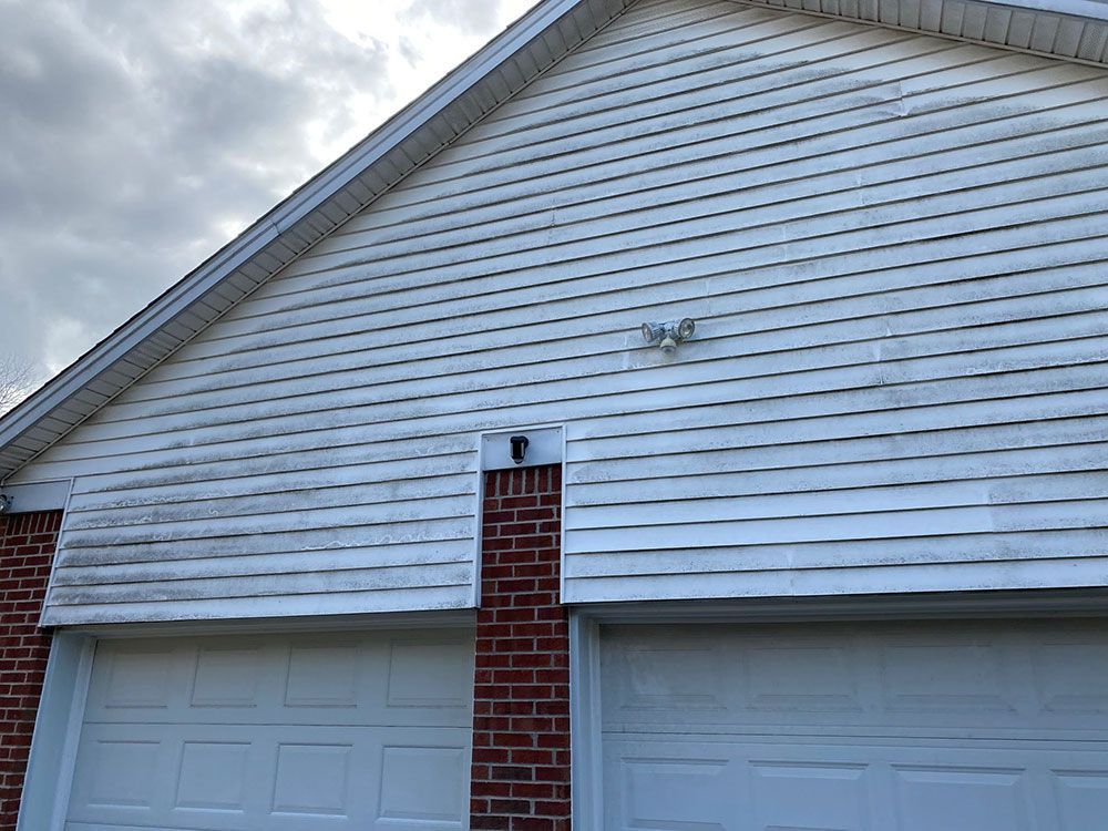 A white house with a brick wall and two white garage doors.