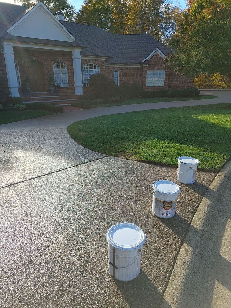 Three buckets of paint are sitting on the sidewalk in front of a house.