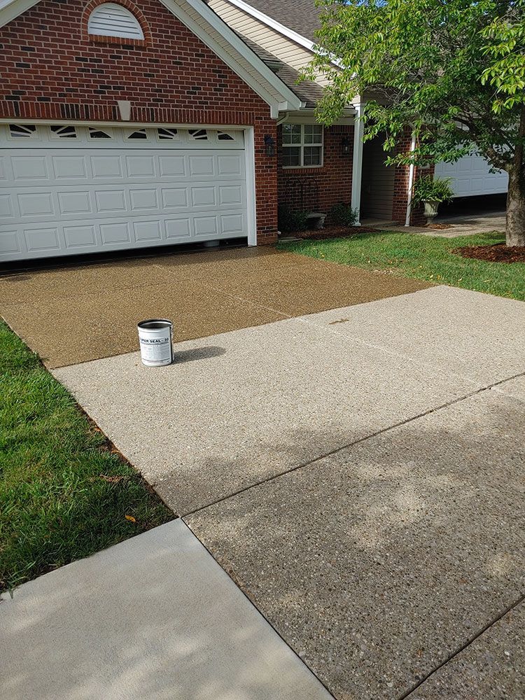 A bucket of paint is sitting on the sidewalk in front of a brick house.