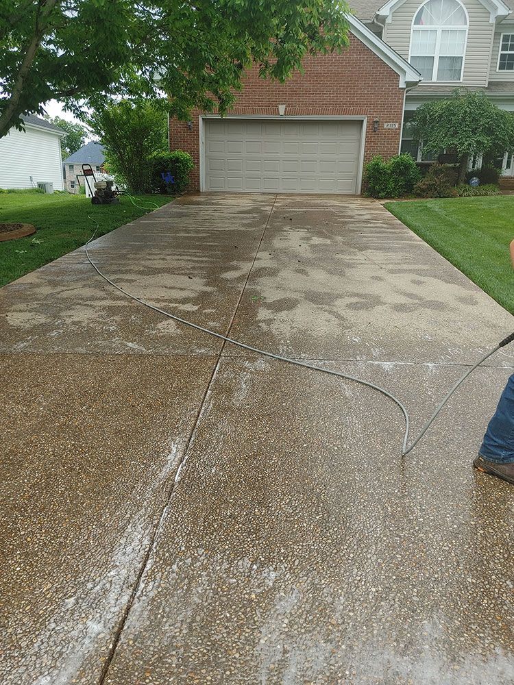 A person is using a pressure washer to clean a driveway in front of a house.