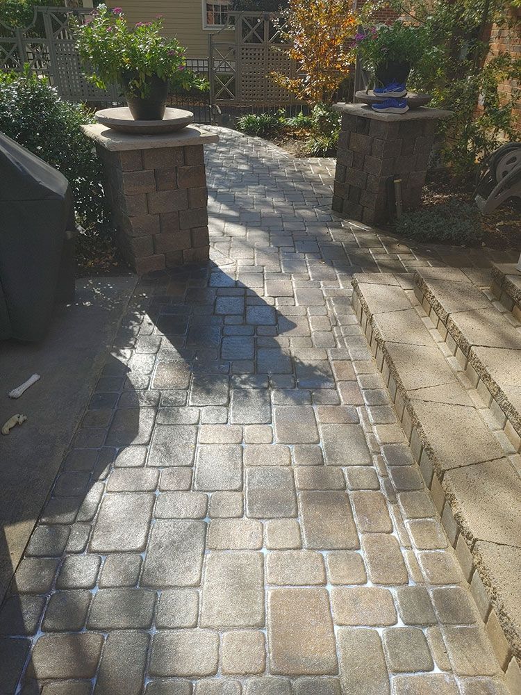 A brick walkway leading to a patio with potted plants on the pillars.