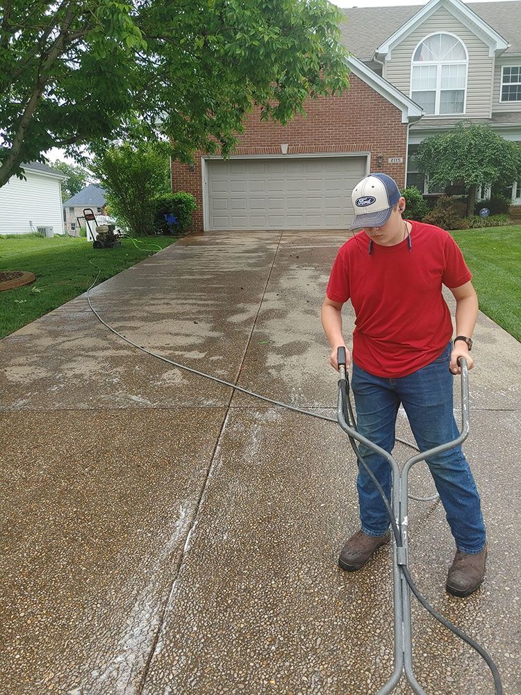 A man is cleaning a driveway with a pressure washer.