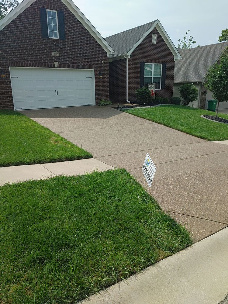 A brick house with a white garage door and a sign in front of it.