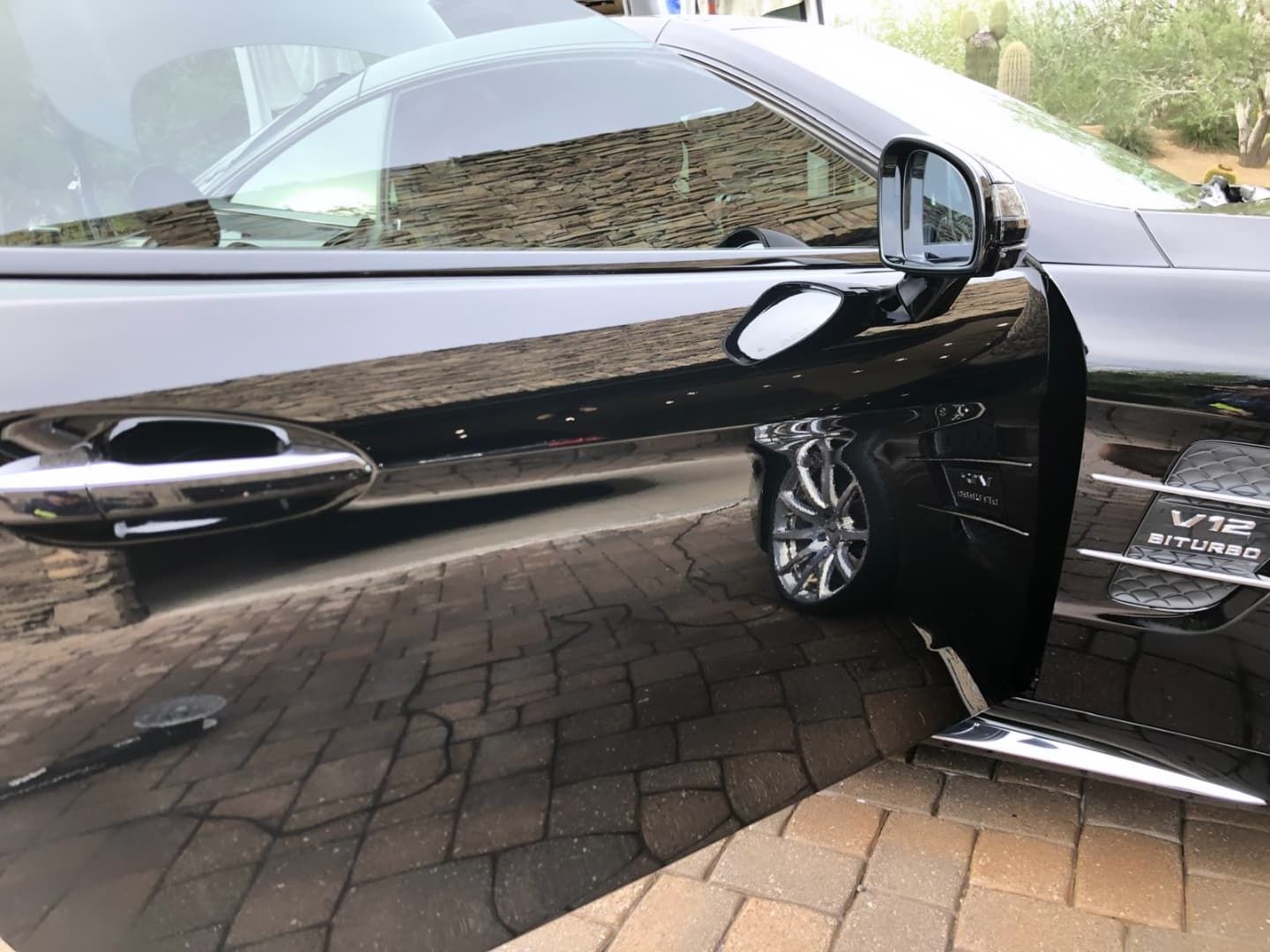 A black car is parked on a brick driveway.