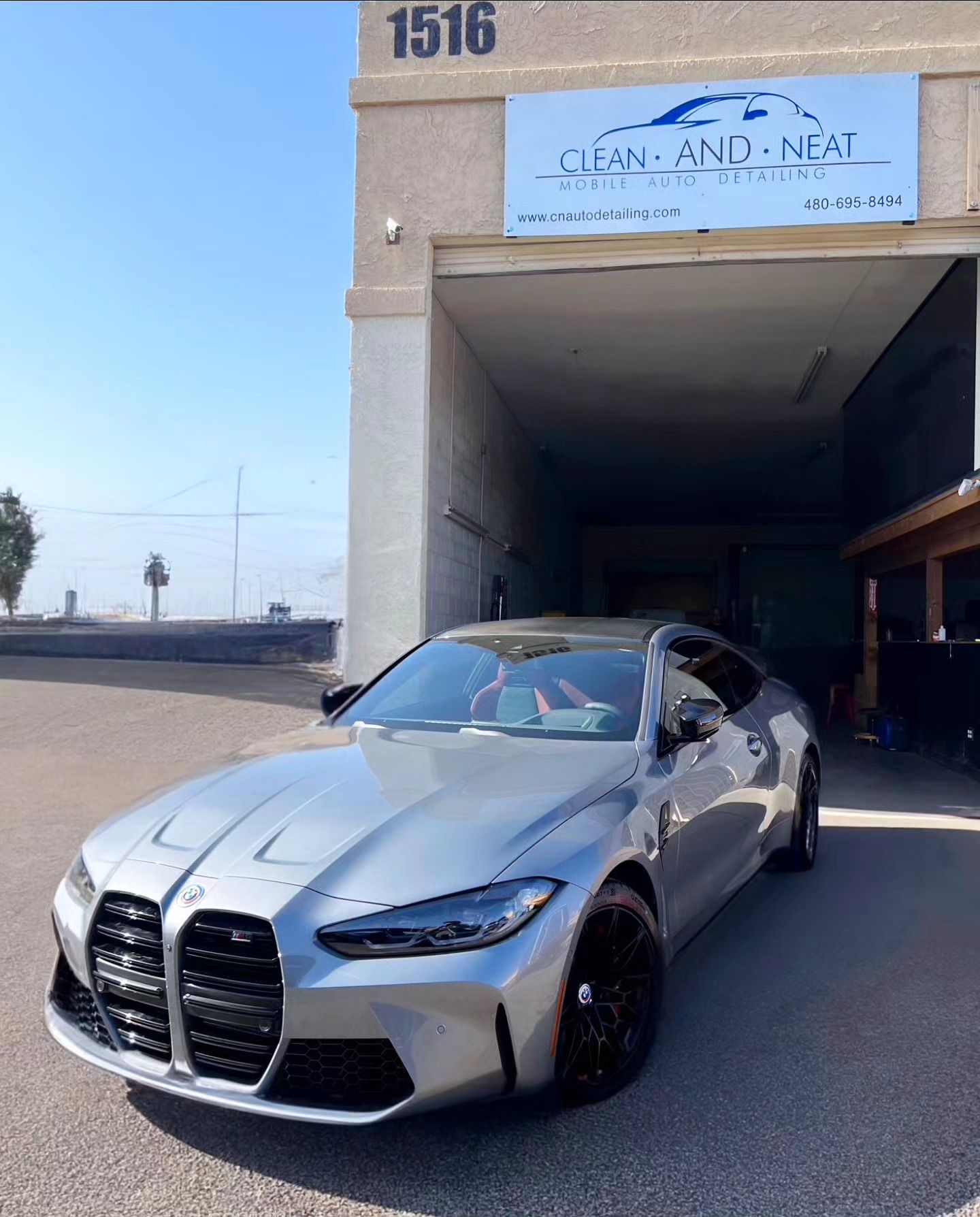 A silver car is parked in front of a building that says clean and neat