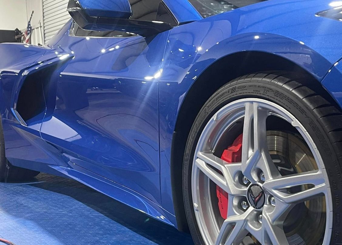 A blue sports car with red brake calipers is parked in a garage.