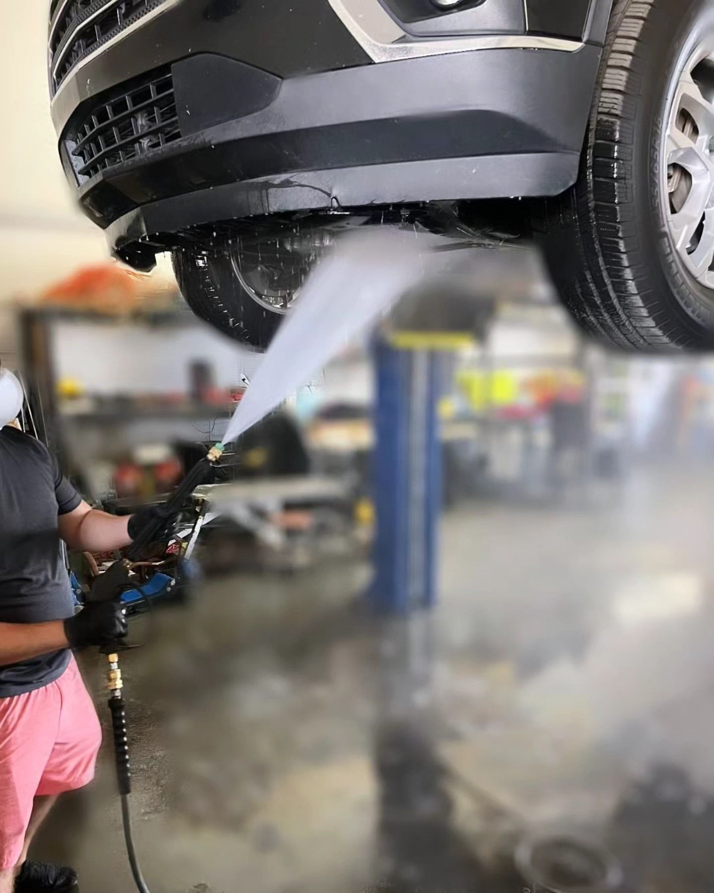 A man is cleaning the underside of a car in a garage.