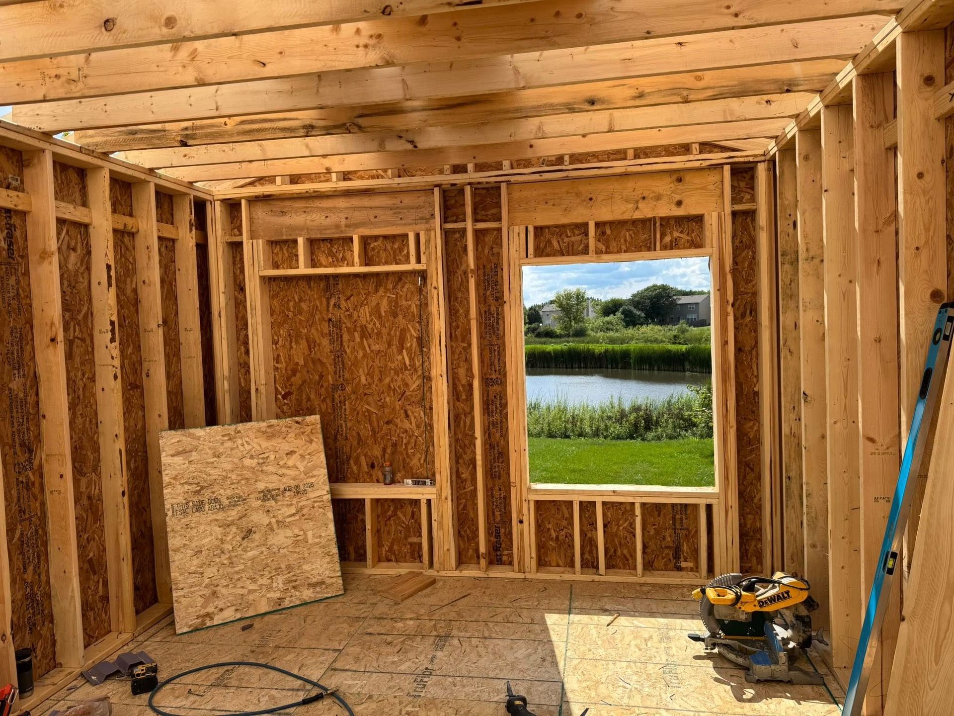 Interior view of a room under construction with wooden framing and a view of a pond through a window.