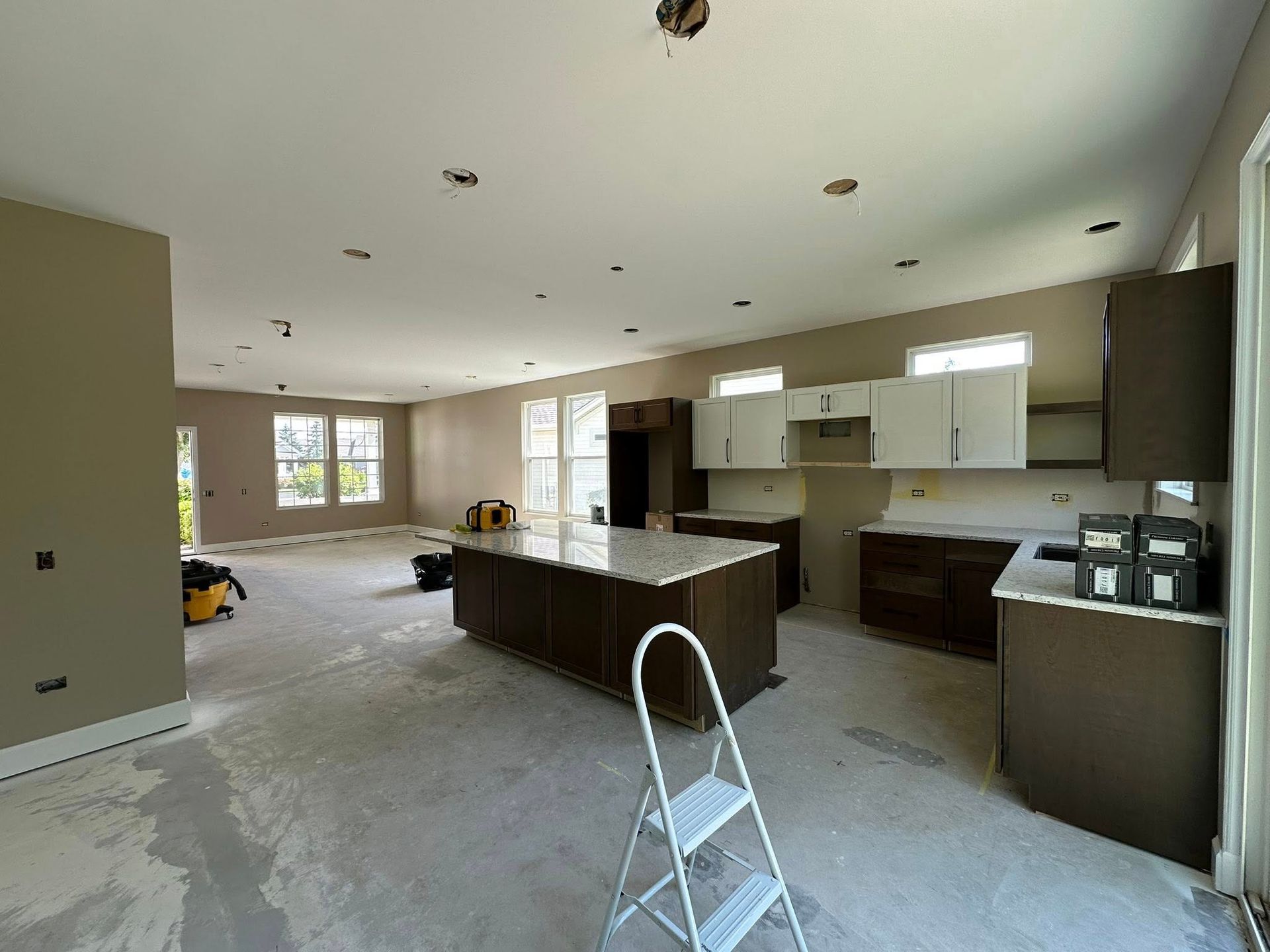 Kitchen undergoing renovation; island, cabinets, and ladder present. Walls are brown and white.