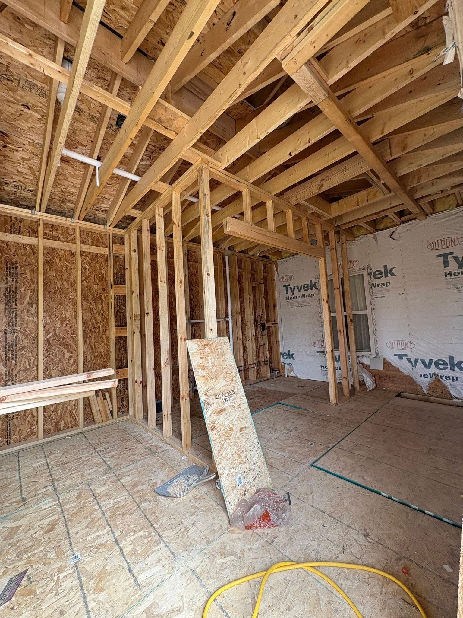 Interior of a building under construction with exposed wooden framing, plywood floors, and Tyvek.