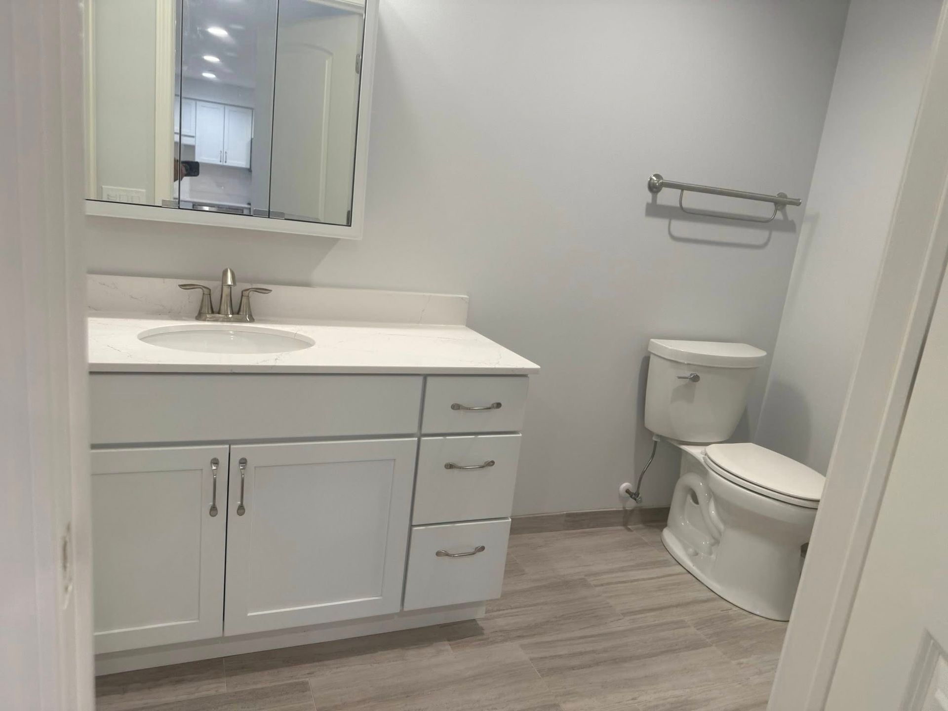 White bathroom with vanity, toilet, and towel rack on a gray-tiled floor.